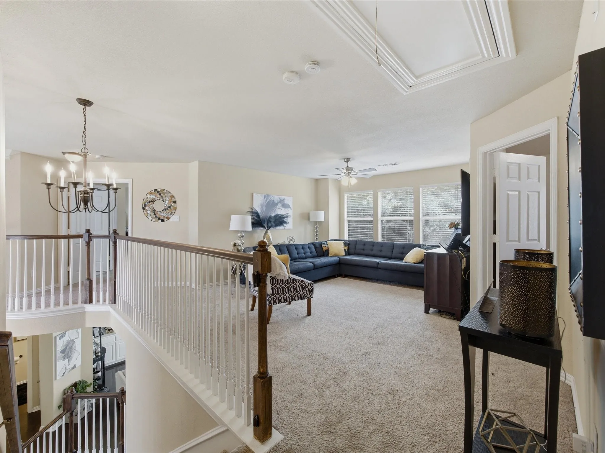 Spacious carpeted upper-level landing featuring a white spindle railing with a dark wood handrail, ample natural light from multiple windows, and a ceiling fan