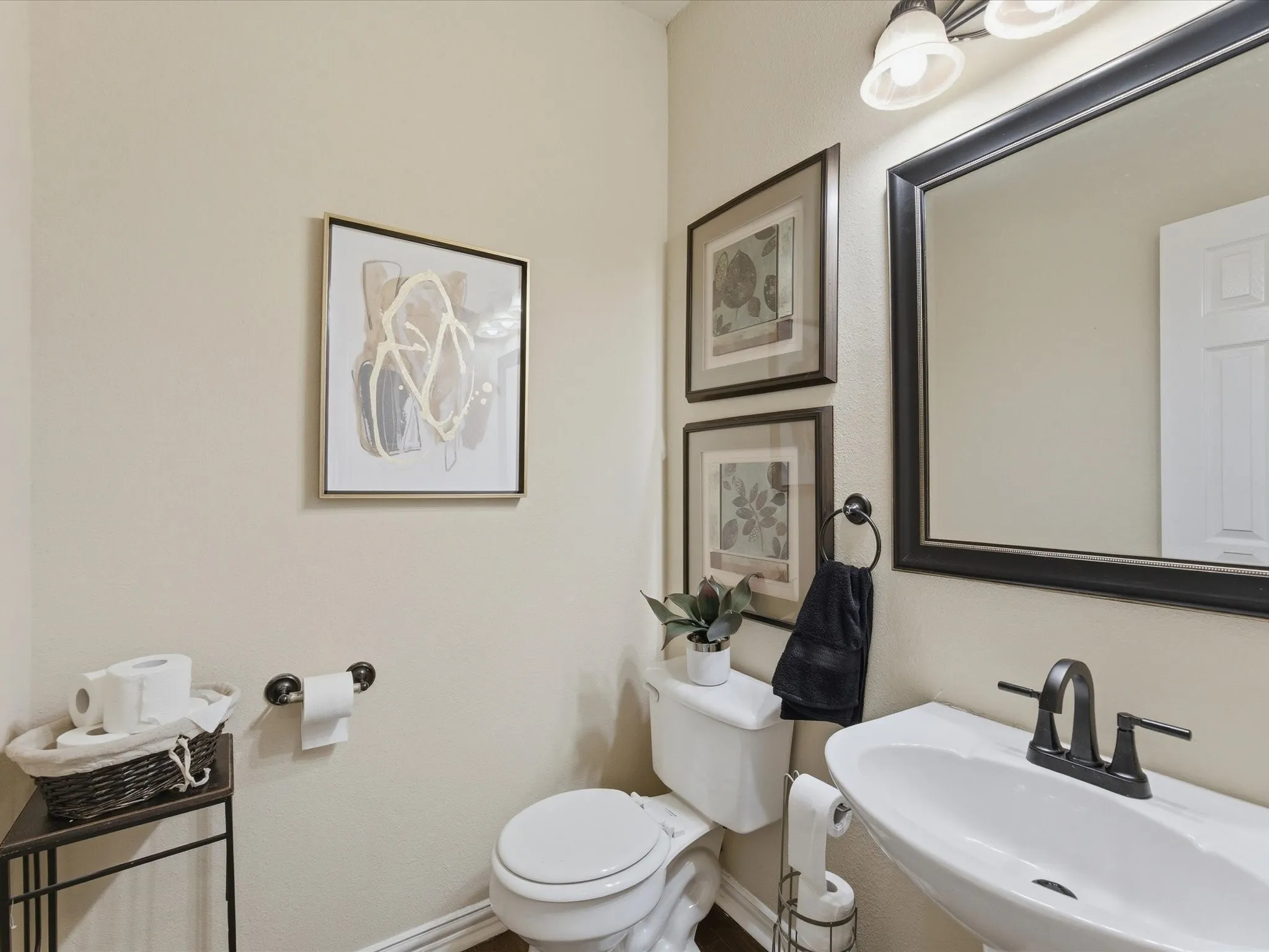 Pedestal sink with a matte black faucet, framed mirror, and coordinating vanity light fixture