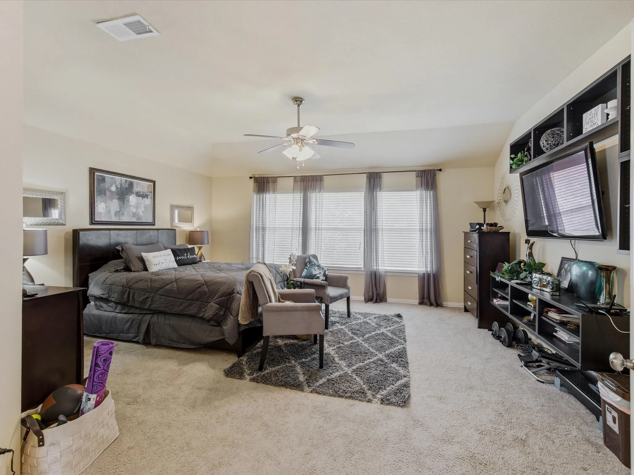 Spacious bedroom featuring light-colored carpeting, multiple windows with blinds and draperies, and a ceiling fan with integrated lighting