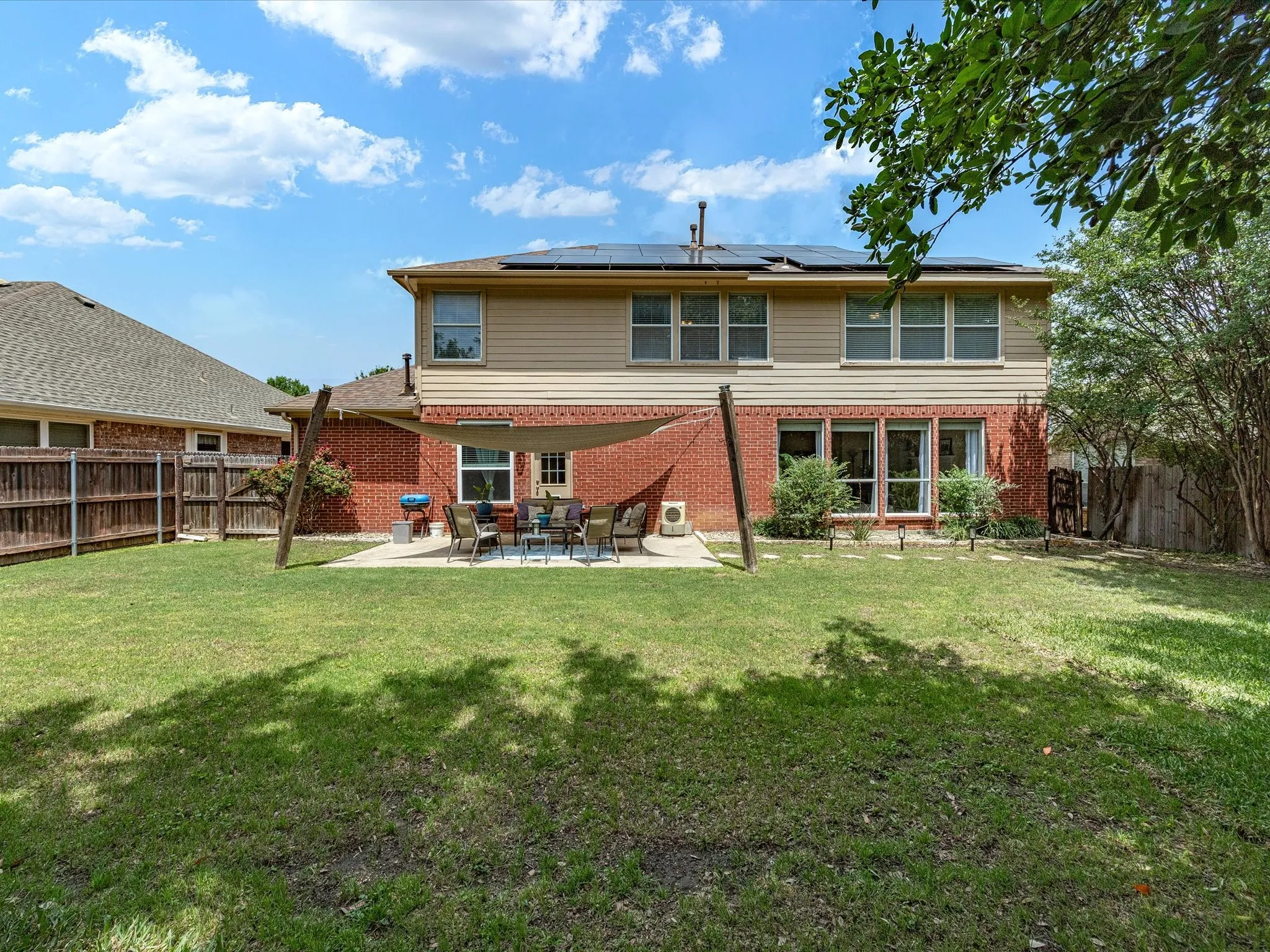 Expansive backyard featuring a large concrete patio, red brick and siding exterior, solar panels, and a wood privacy fence