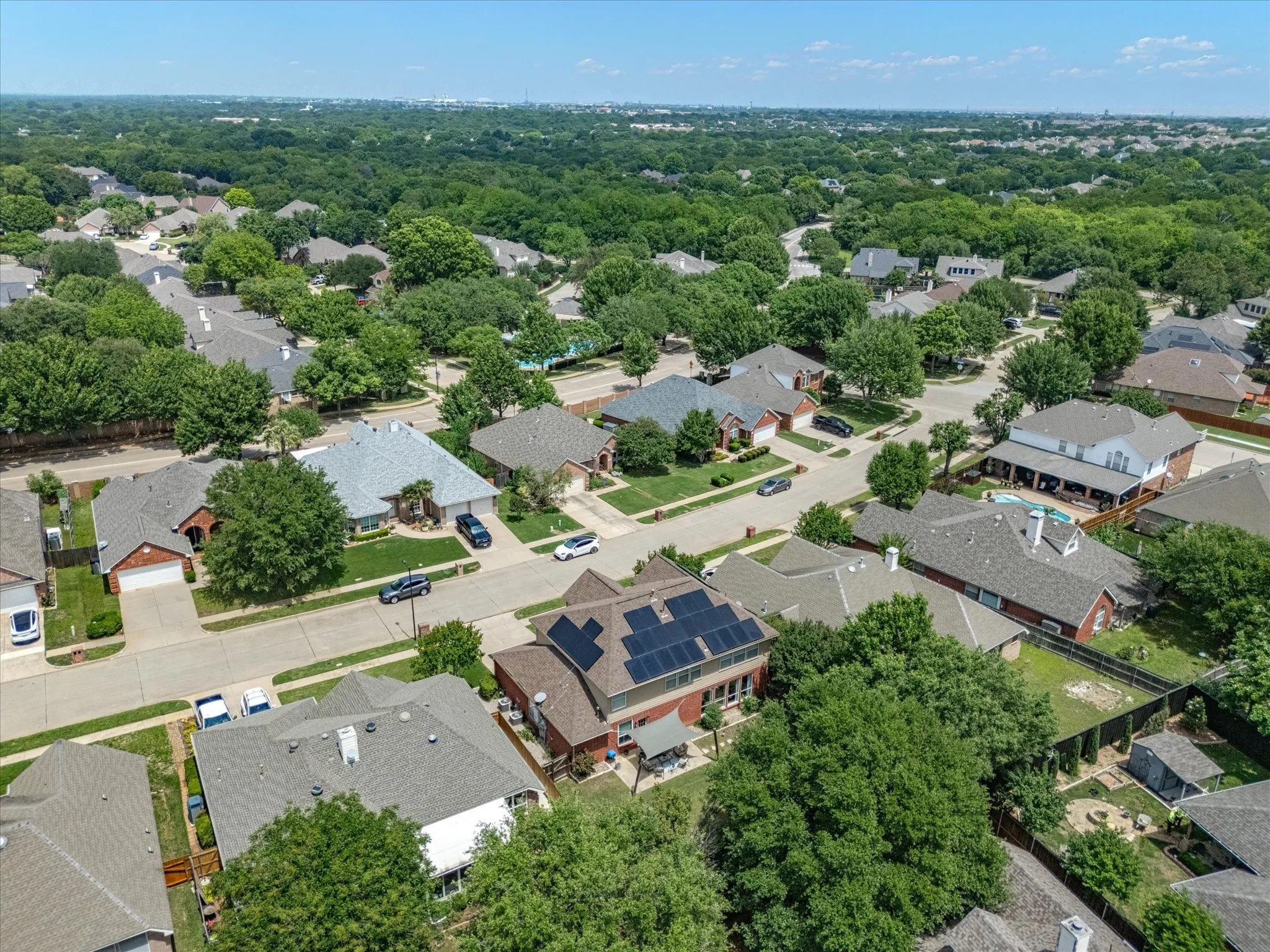 Residential neighborhood featuring mature tree canopy, varied architectural styles, and a property with rooftop solar panels