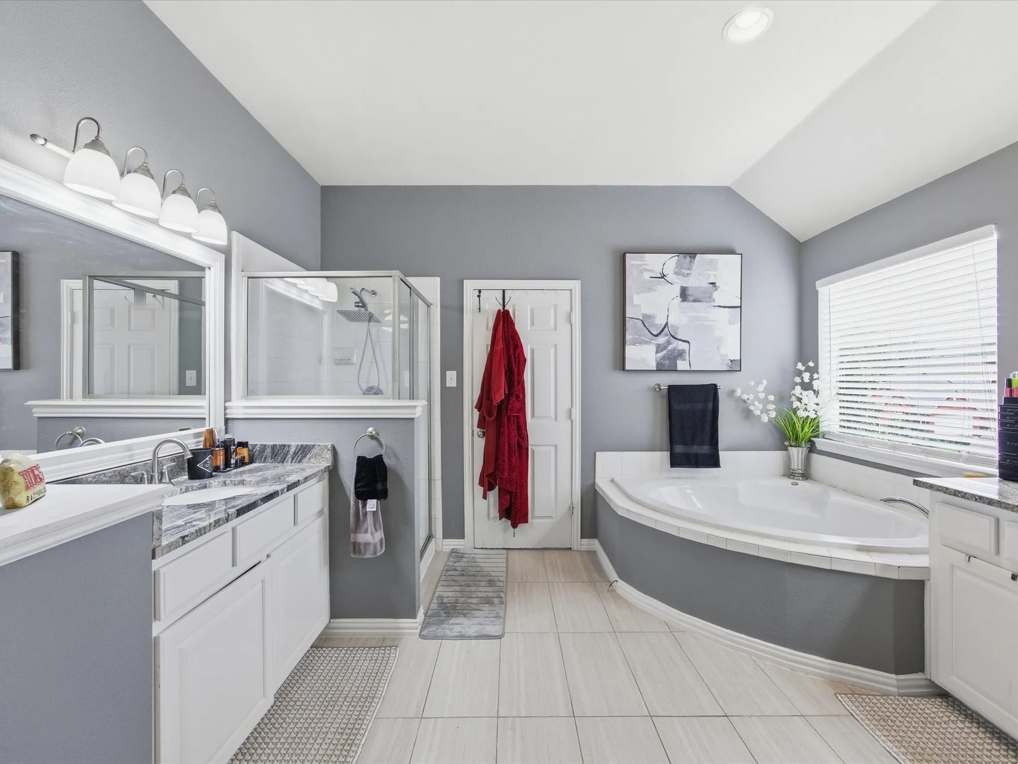 Bathroom featuring a corner soaking tub, a walk-in shower with glass enclosure, and a double vanity with stone countertop and dual sinks
