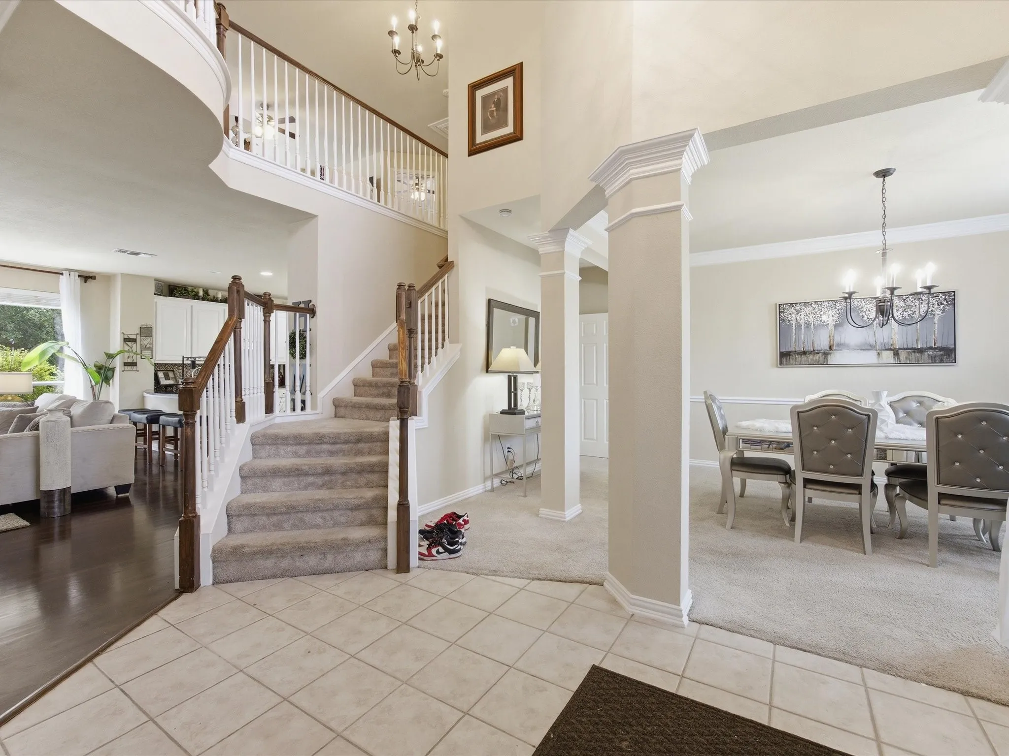Two-story foyer with a grand staircase featuring wood banisters and white spindles, tile flooring, and an overhead chandelier