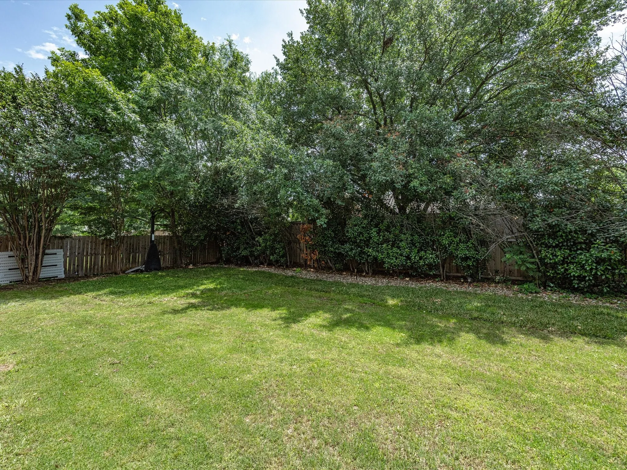 Expansive lawn area bordered by a wood privacy fence and mature trees