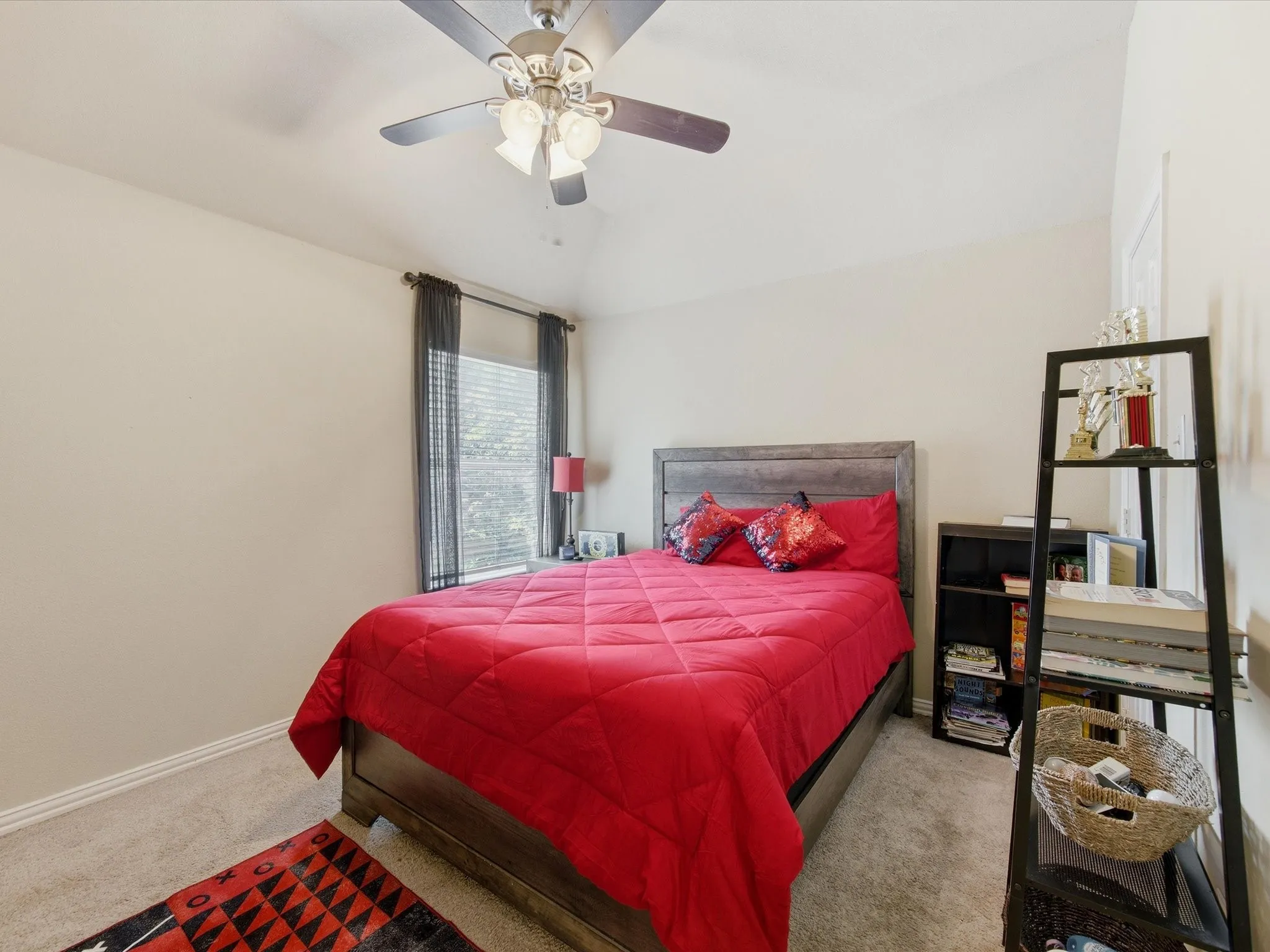Carpeted room featuring a ceiling fan with integrated lighting, a window with blinds and dark curtains, and a built-in shelf unit
