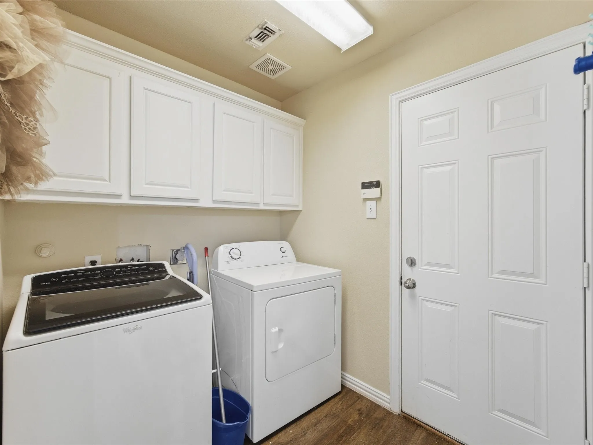 Laundry area with white upper cabinetry, wood-finish flooring, and a paneled exterior door