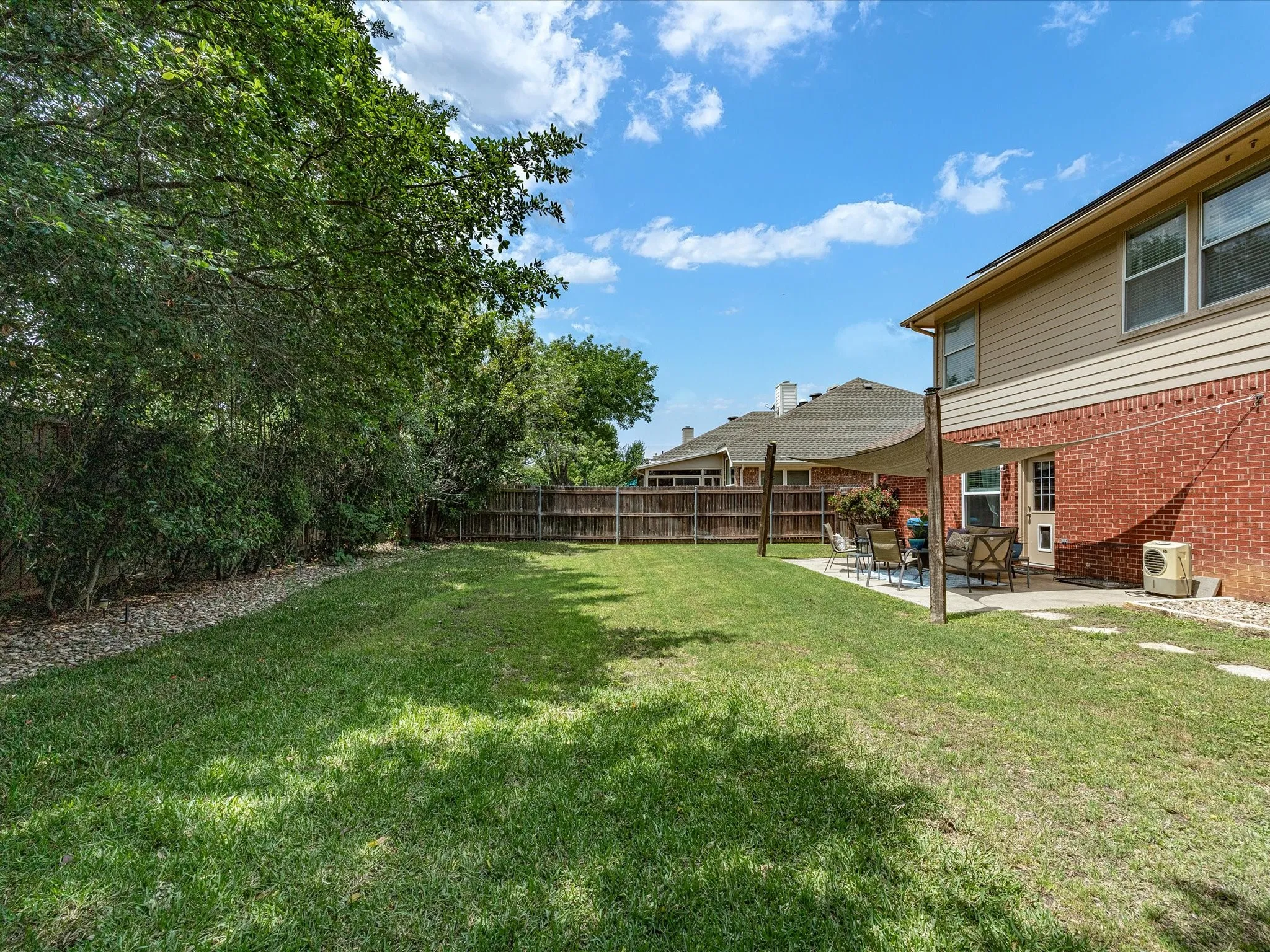 Expansive fenced backyard featuring a spacious lawn, mature trees, a concrete patio, and a shade sail structure