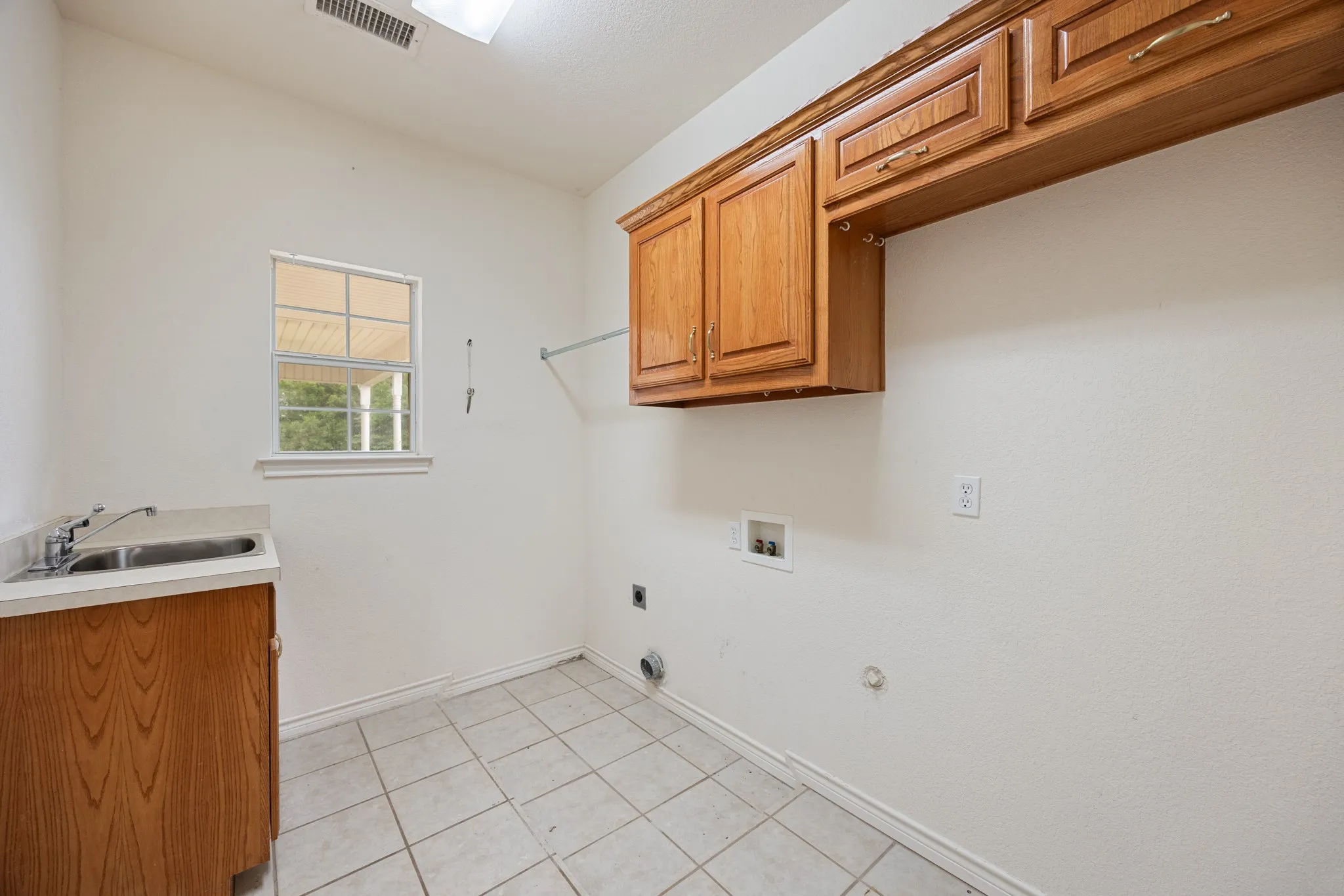 Utility room featuring tiled flooring, a window, wood cabinetry, an integrated sink with a countertop, and a clothes hanging rod