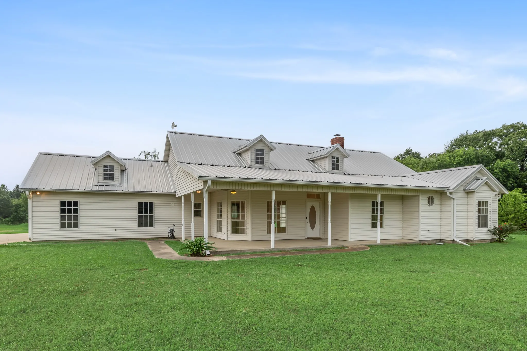 Ranch-style residence featuring white horizontal siding, a covered front porch, multiple dormer windows, and a gray metal roof
