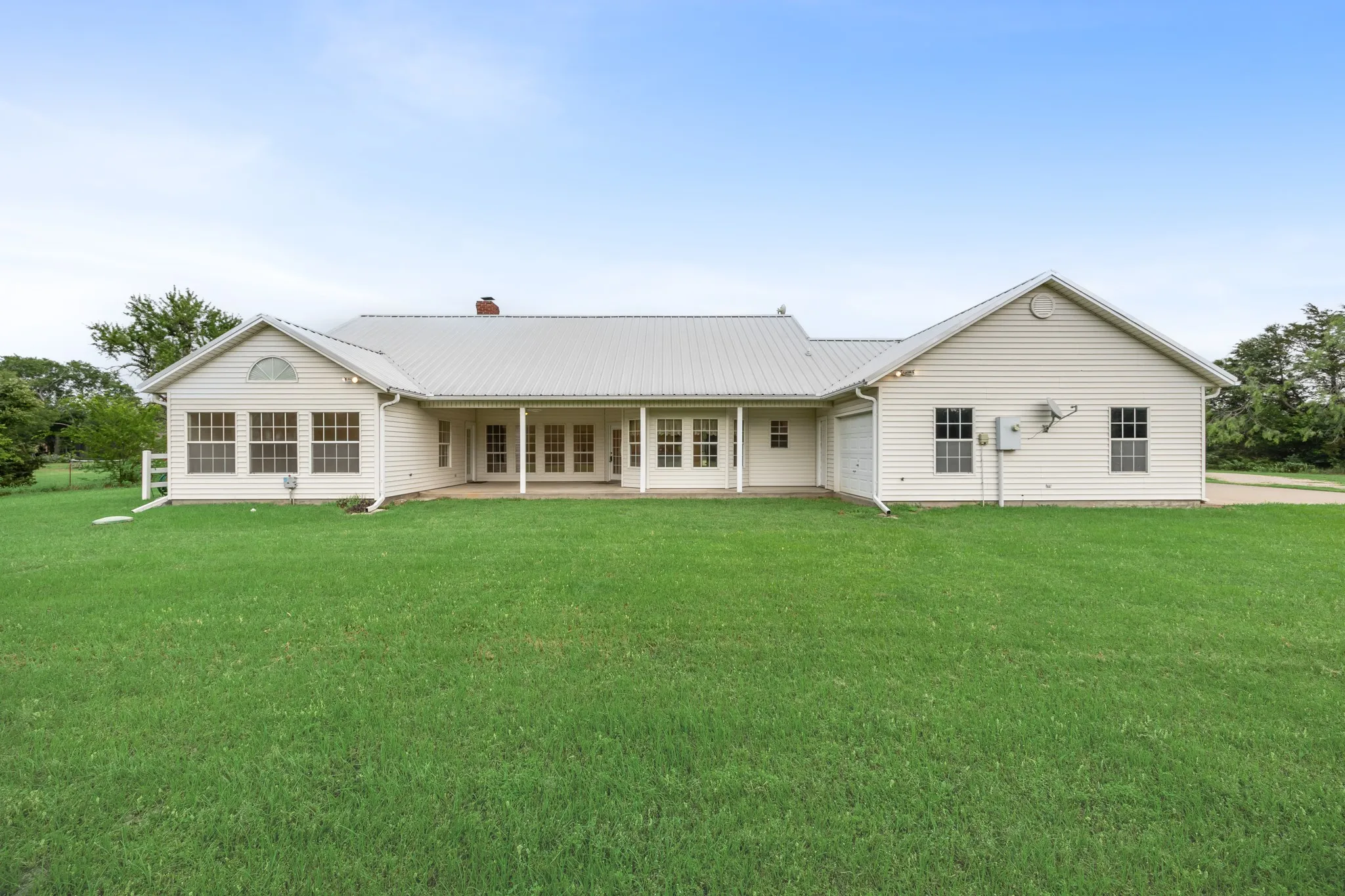 Expansive lawn with a white siding exterior featuring a covered porch, a sunroom with an arched transom window, a metal roof, and an attached garage