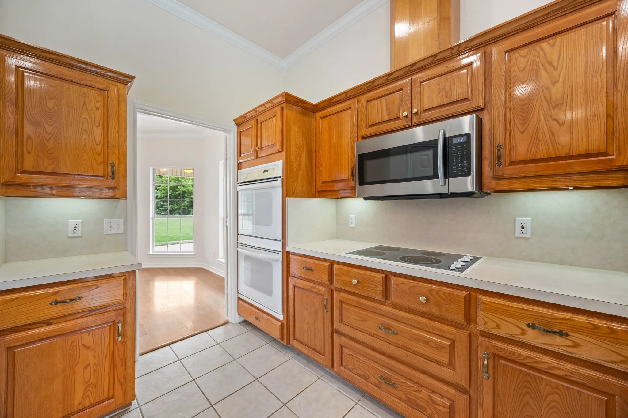 Kitchen featuring wood cabinetry with brass hardware, stainless steel microwave, electric cooktop, double wall ovens, and light-toned countertops