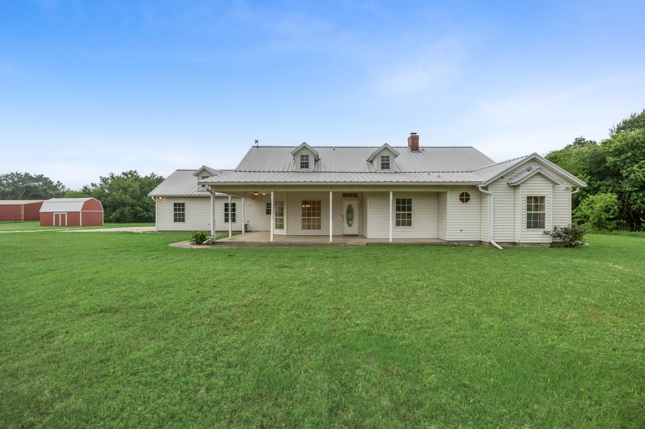 Spacious single-story residence featuring white siding, a metal roof, and an inviting front porch