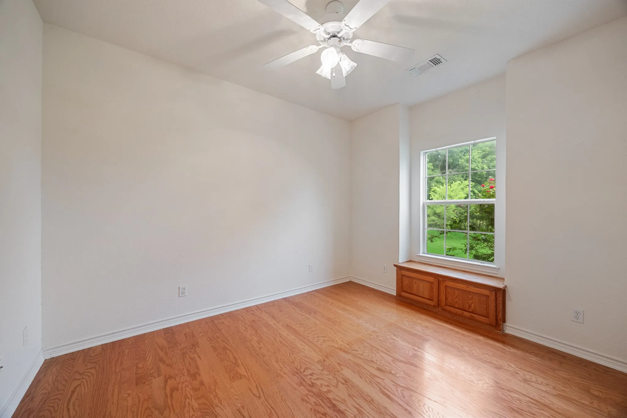 Room featuring wood-finish flooring, a window with exterior tree scenery, and a built-in wood window seat with cabinetry
