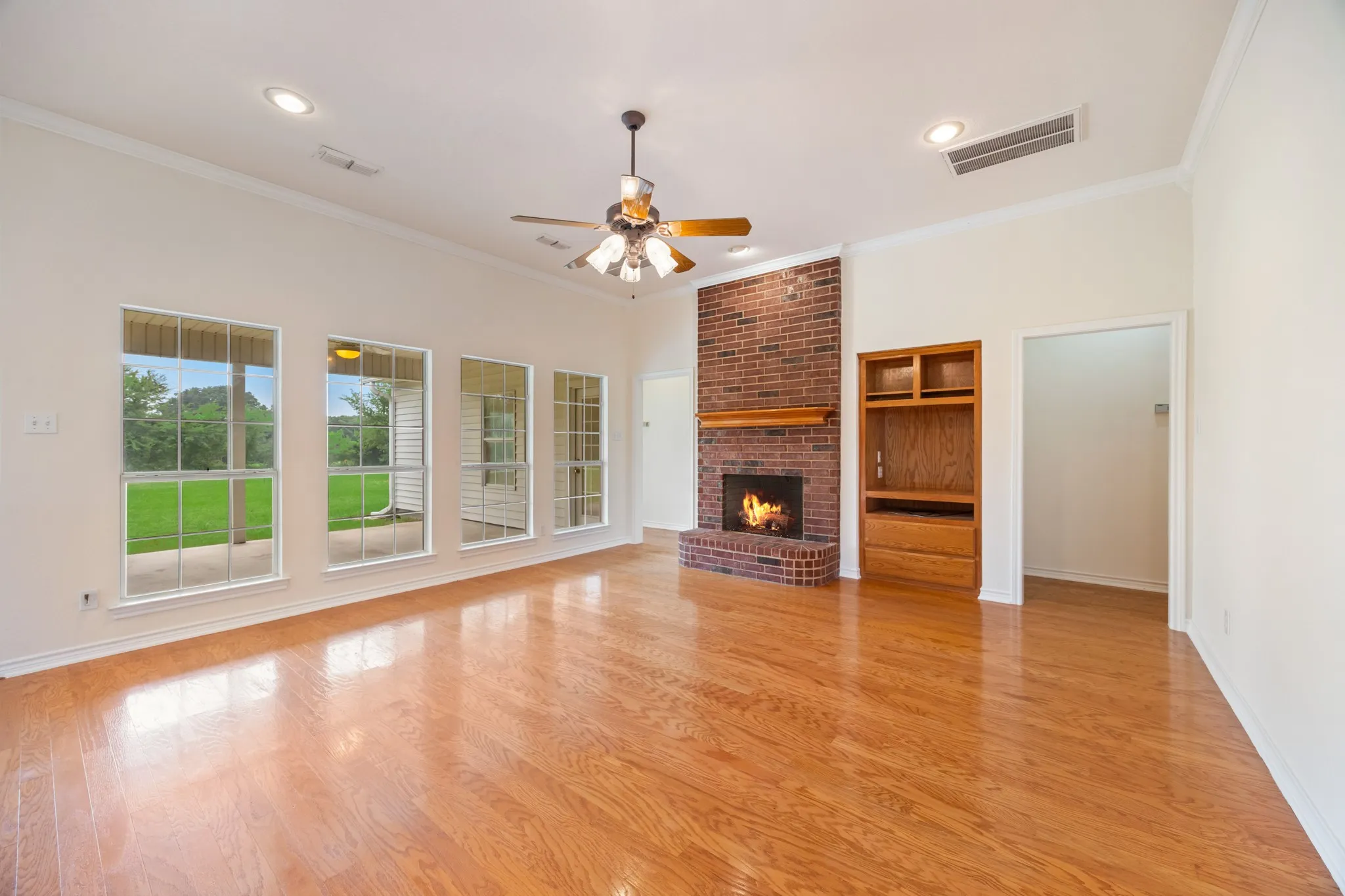 Spacious living area featuring wood-finish flooring, a brick fireplace with a wood mantle, and an integrated wood entertainment center