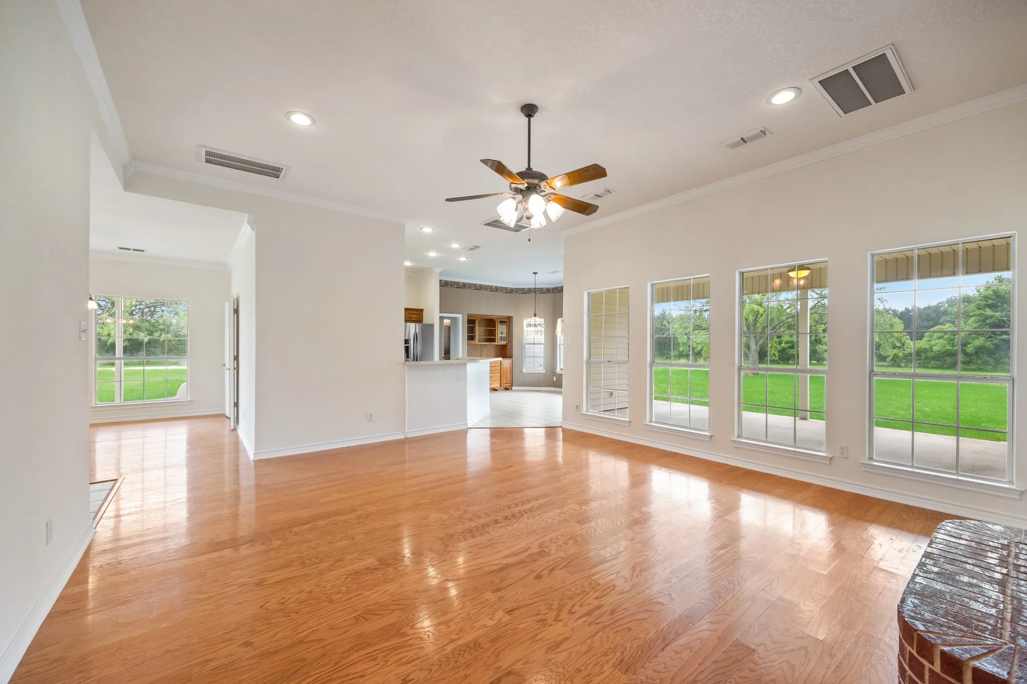 Spacious living area featuring wood-finish flooring, ample natural light from multiple windows, recessed lighting, and a ceiling fan