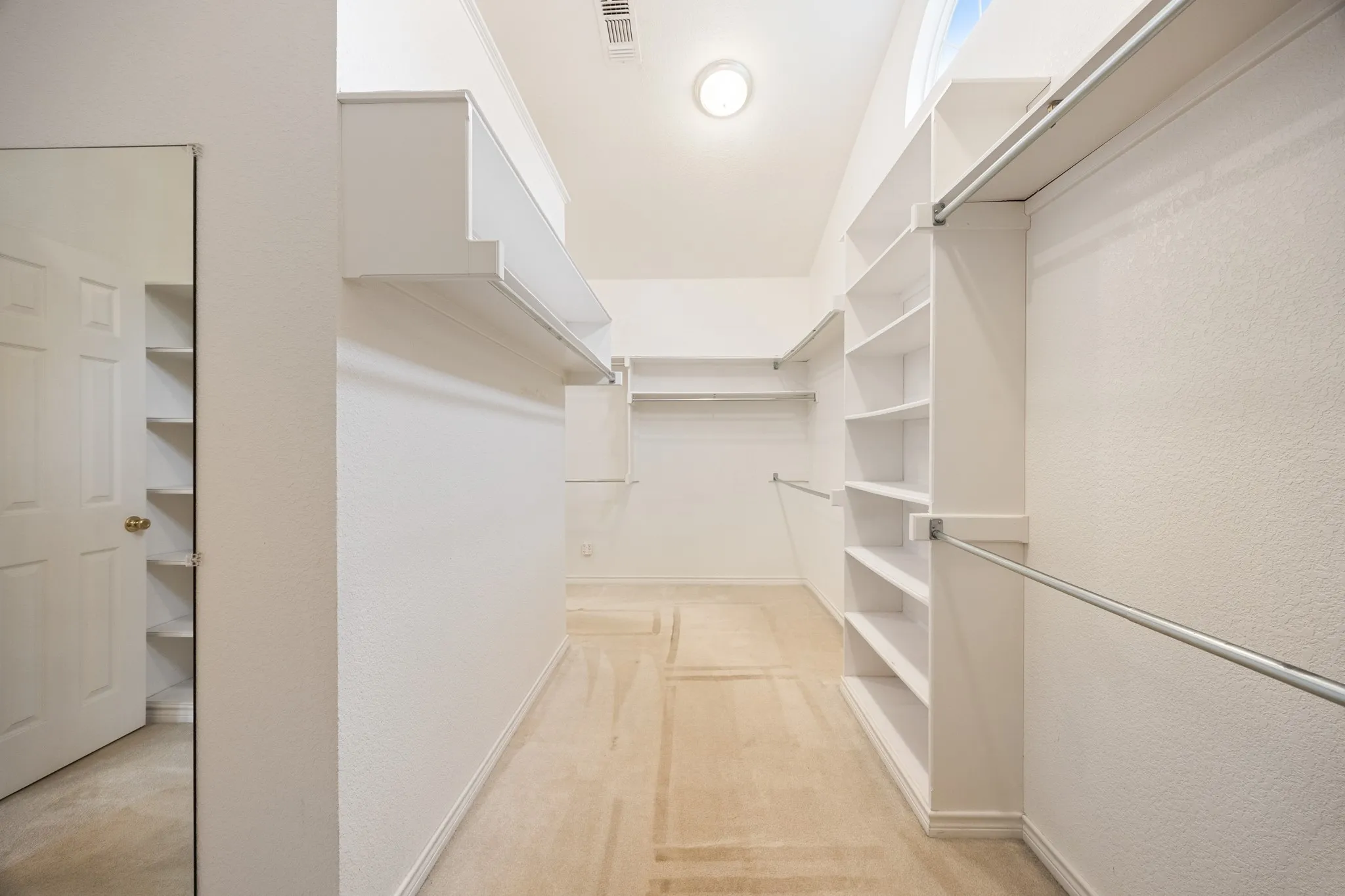 Walk-in closet featuring extensive built-in shelving, multiple hanging rods, and light-toned carpet flooring