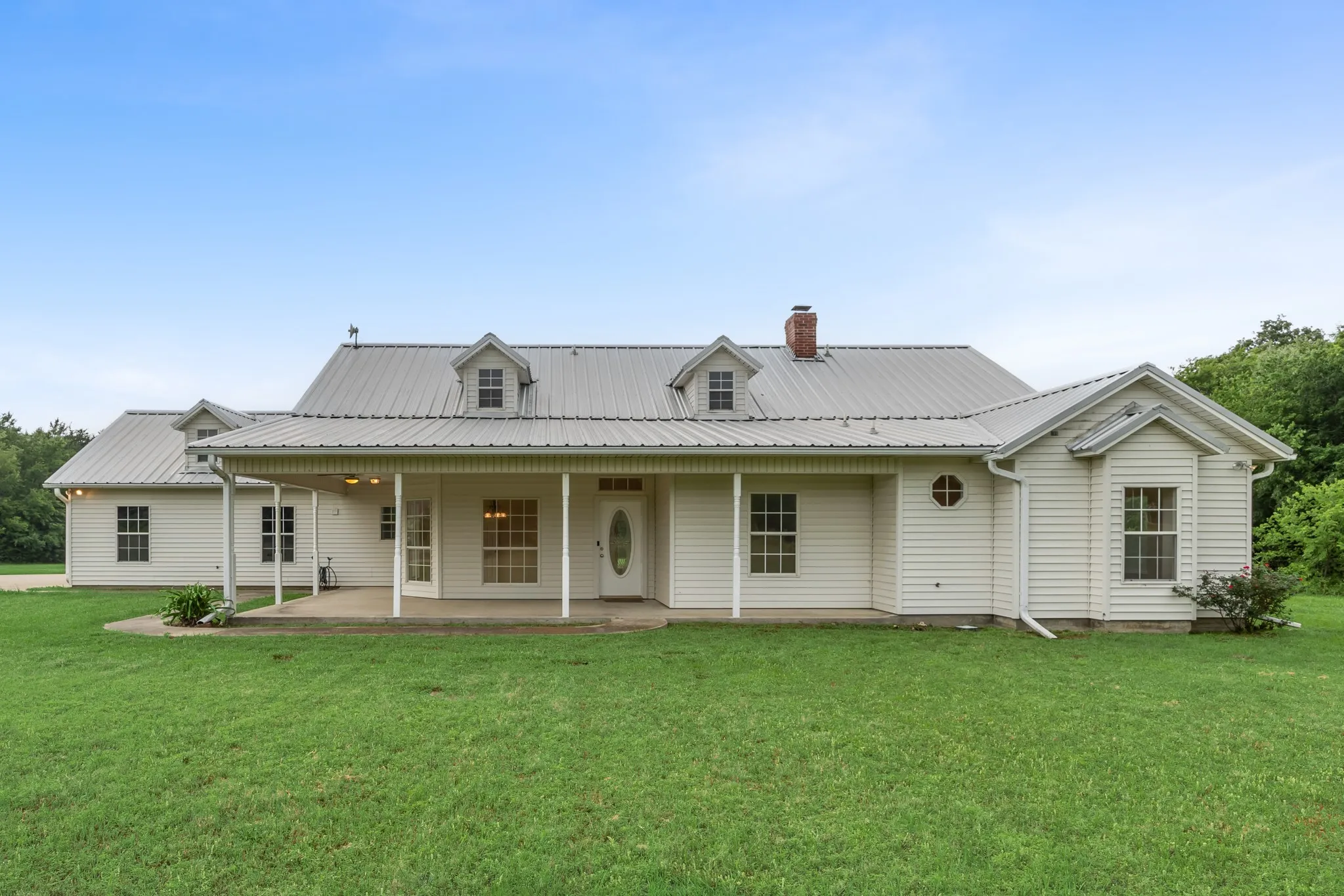 White siding exterior with a metal roof, dormer windows, and an expansive covered porch