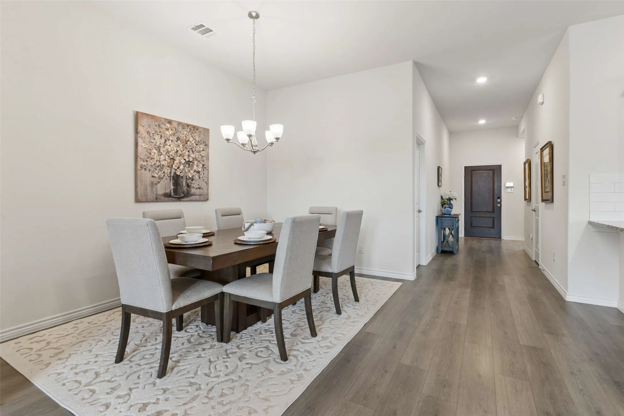 Open-concept dining area featuring a contemporary chandelier, light wood-finish flooring, and a dark wood entry door