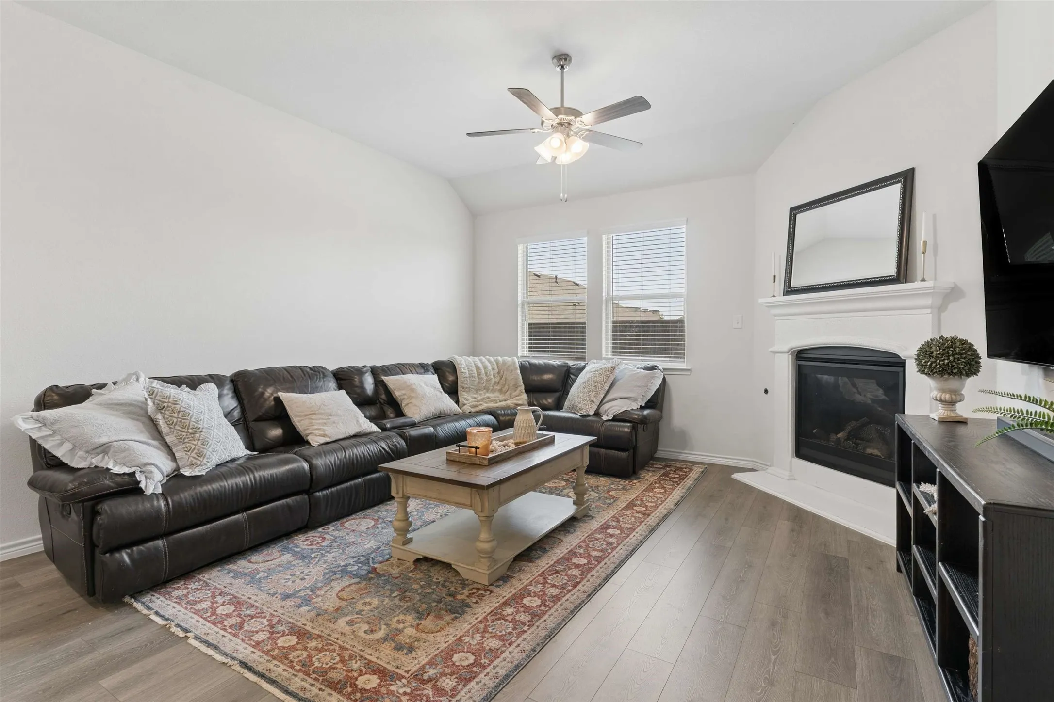Living area featuring wood-finish flooring, a white mantel fireplace, and vaulted ceilings
