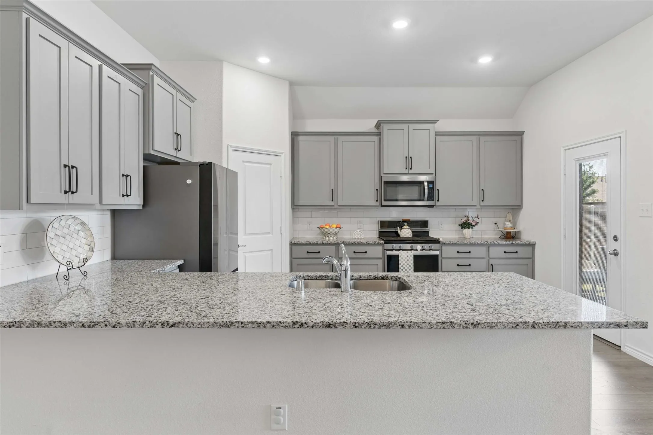 Kitchen featuring light gray cabinetry with dark hardware, granite countertops, a white subway tile backsplash, and recessed lighting