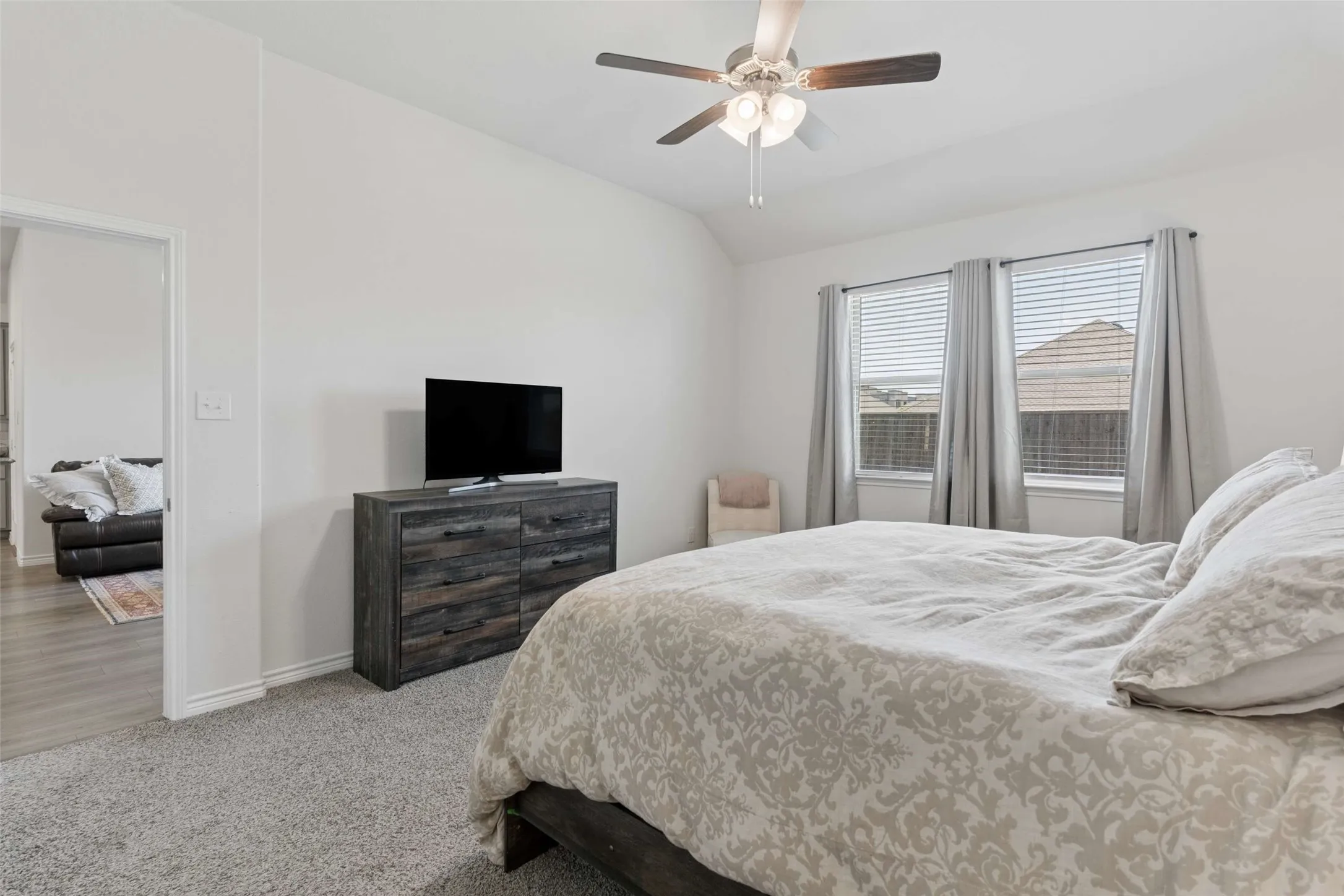 Carpeted bedroom featuring two windows with blinds, a ceiling fan with light fixture, and an open doorway to another interior space