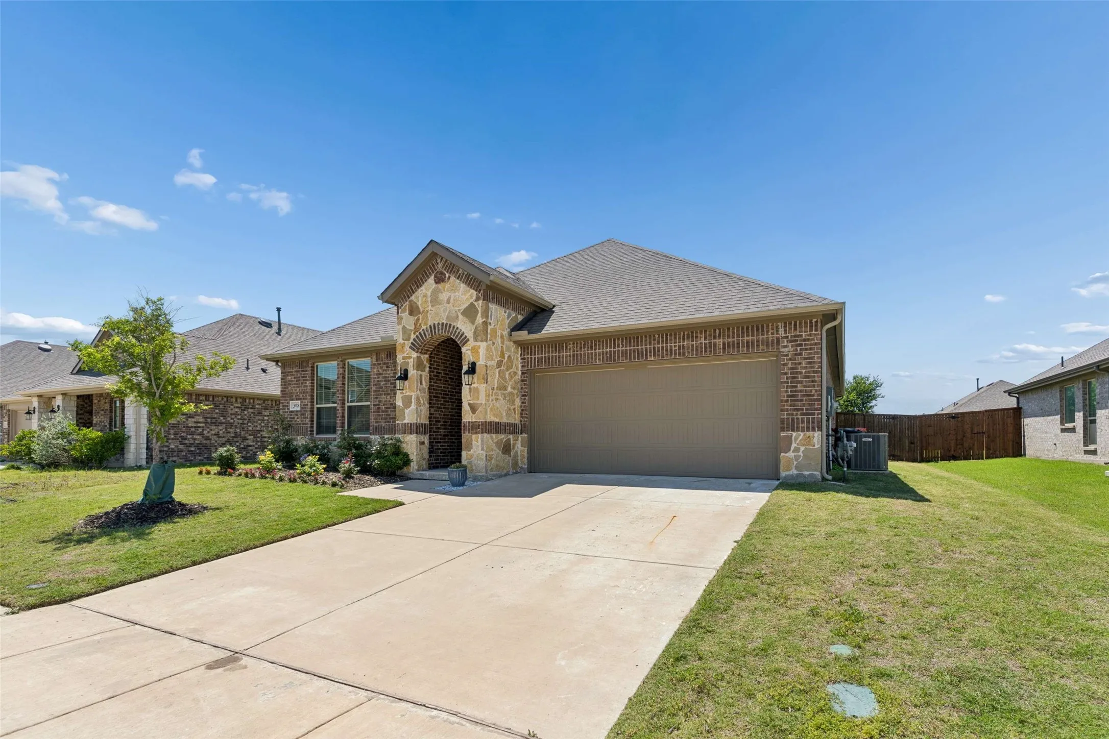 Brick and stone facade residence featuring an arched entry, two-car garage, and established landscaping