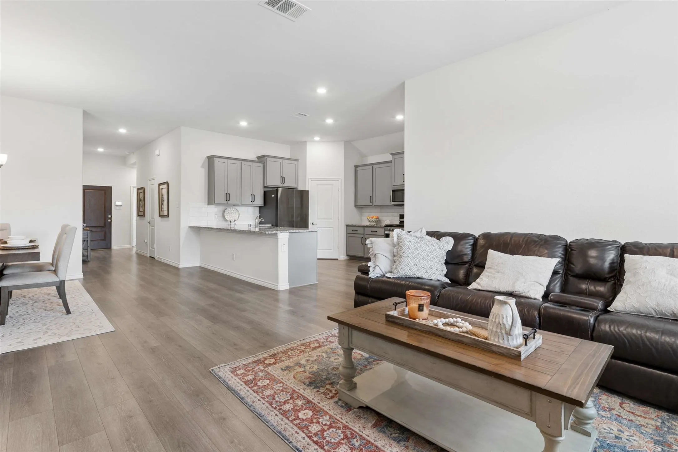 Open-concept living area featuring wood-finish flooring, recessed lighting, and a kitchen with gray cabinetry, dark appliances, and a white subway tile backsplash