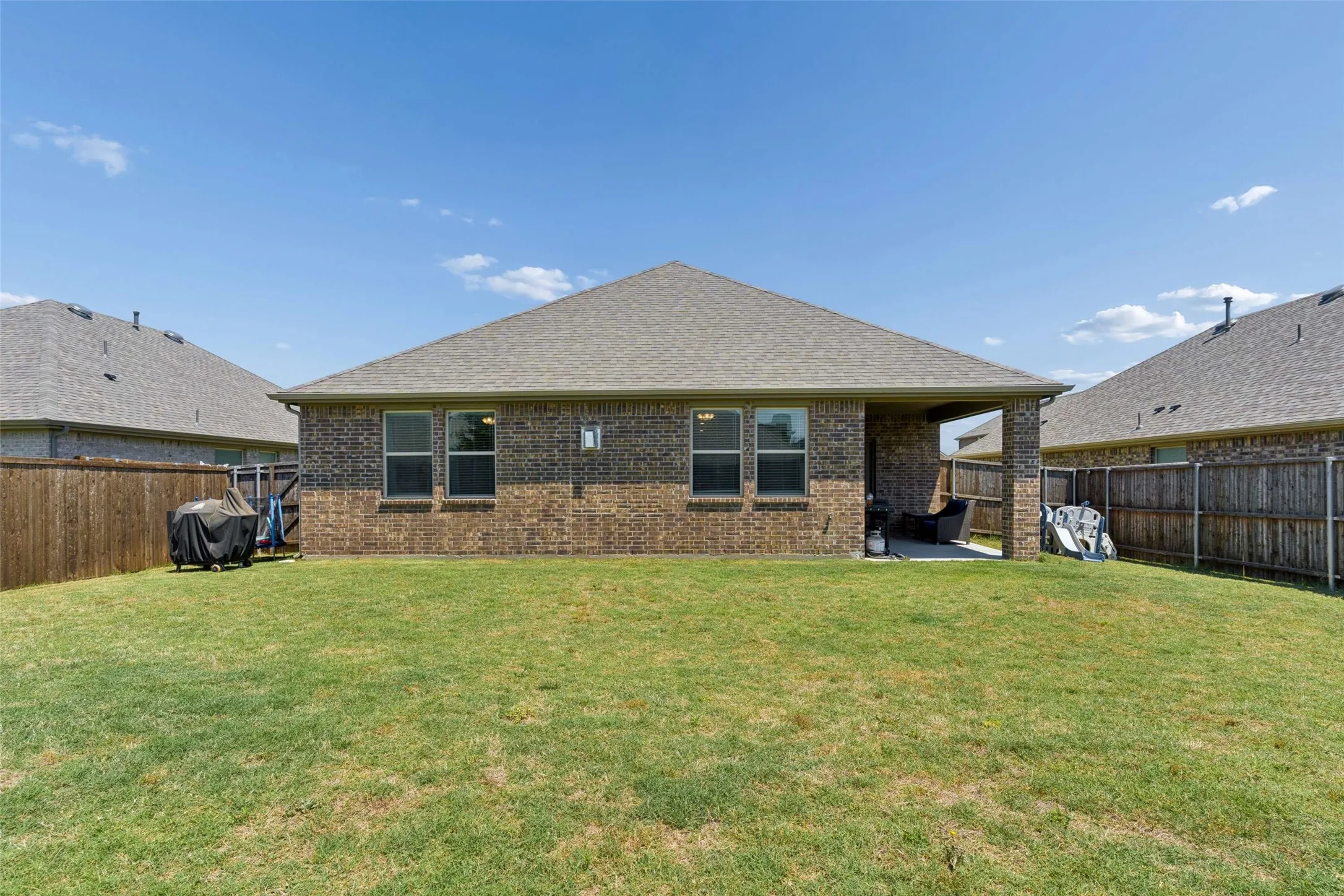 Expansive backyard with a manicured lawn, brick exterior, and covered patio