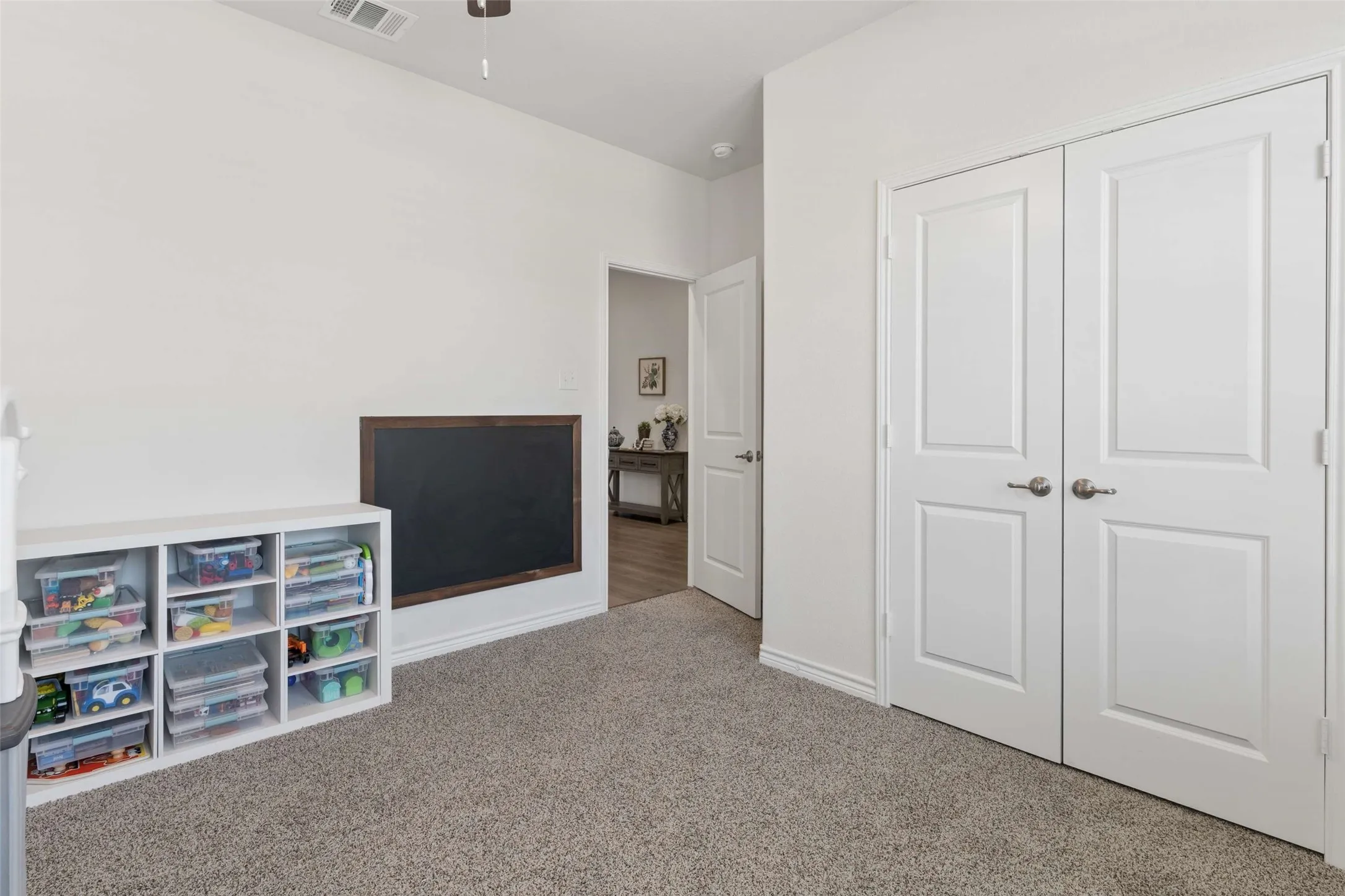 Carpeted room featuring a built-in framed chalkboard, white baseboards, and white bi-fold closet doors with brushed nickel hardware