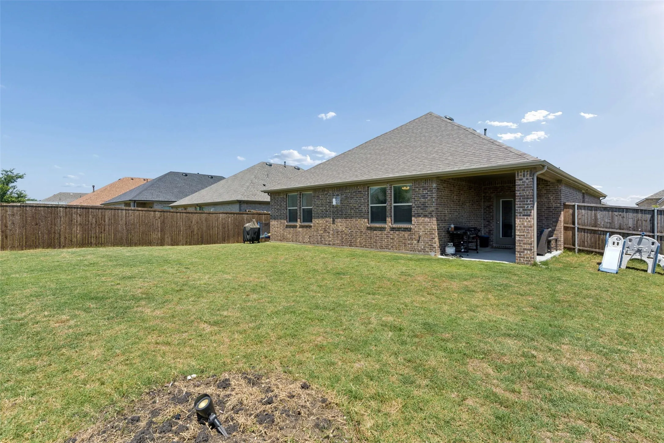 Expansive backyard with a manicured lawn, full wood privacy fencing, and a covered concrete patio