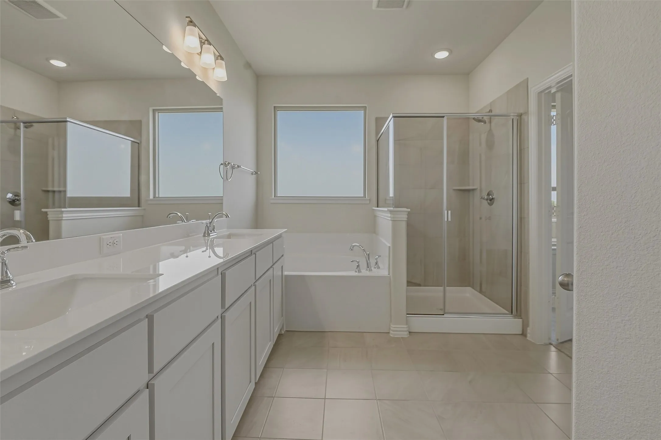 Spacious bathroom featuring a dual vanity with white cabinetry and countertops, a large soaking tub, a separate glass-enclosed shower with tiled walls, and large format tile flooring