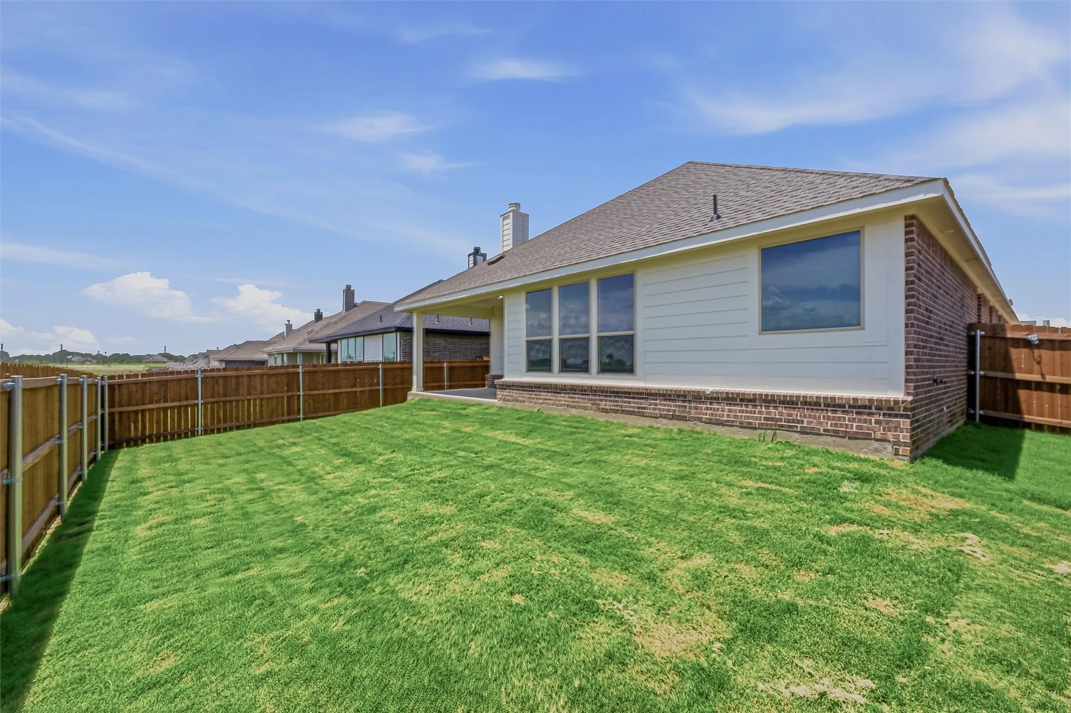 Expansive backyard featuring a lush lawn, privacy fencing, and a covered patio