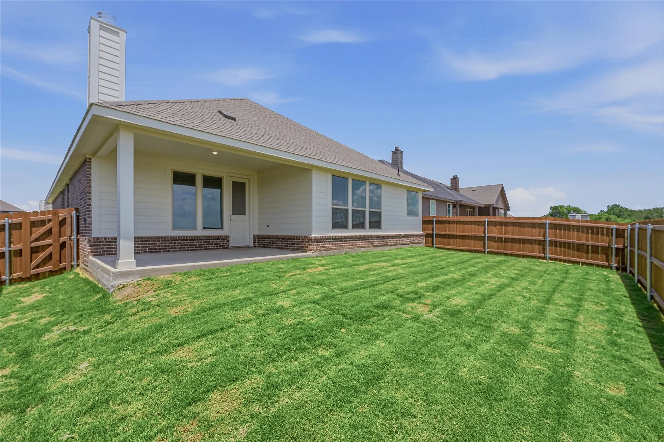 Expansive backyard featuring a manicured lawn, full wood fencing, and a covered patio with concrete flooring