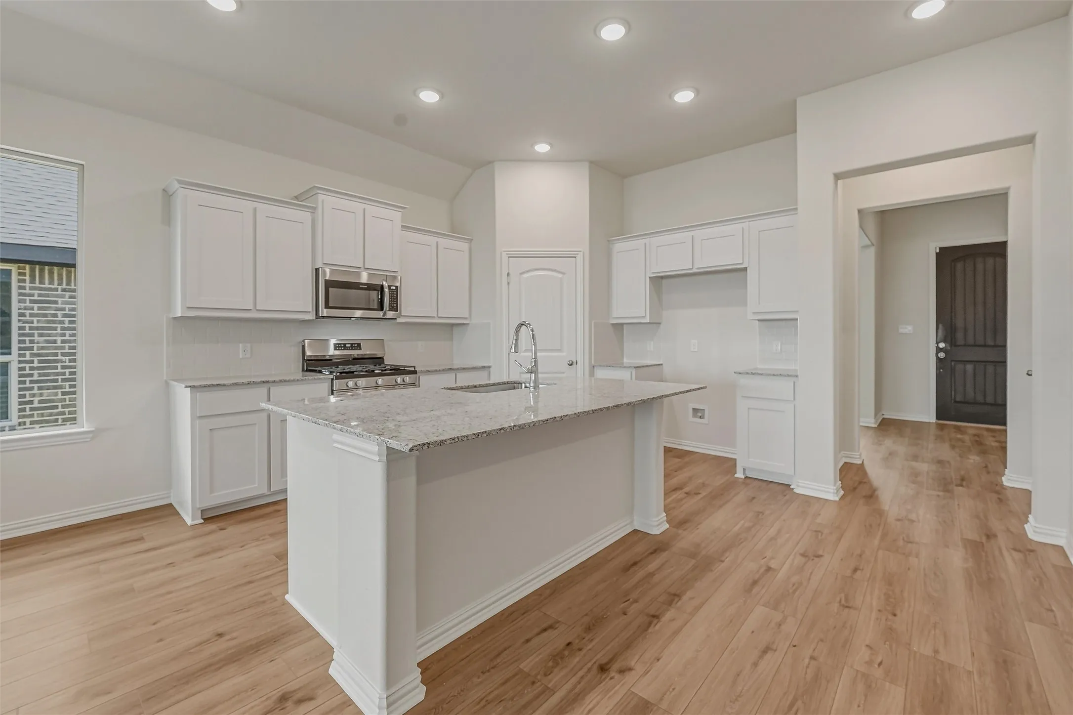 Kitchen featuring a central island with a granite countertop, white cabinetry, stainless steel appliances, and wood-finish flooring