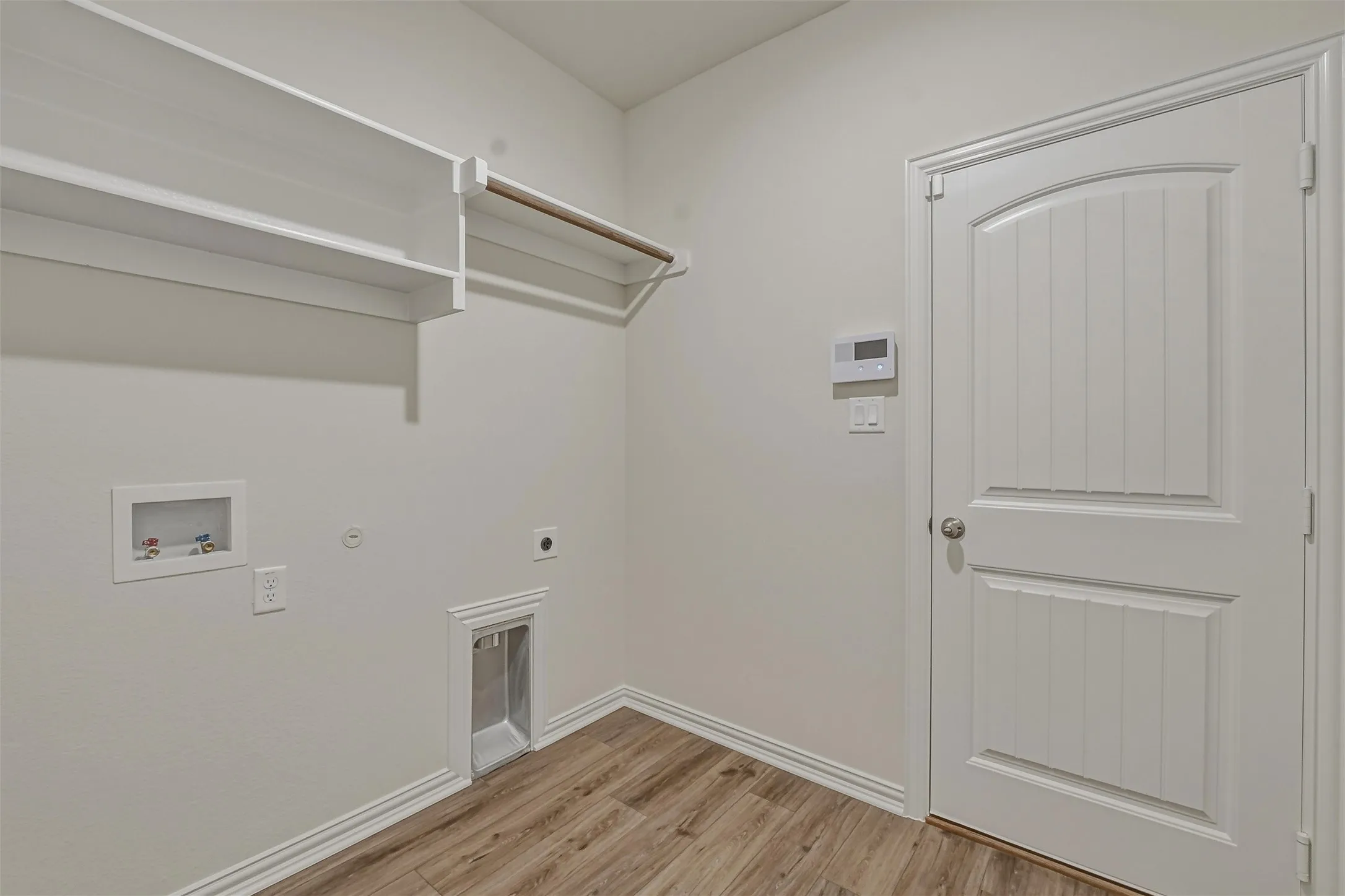 Dedicated utility space featuring built-in shelving, a clothes hanging rod, and wood-finish flooring