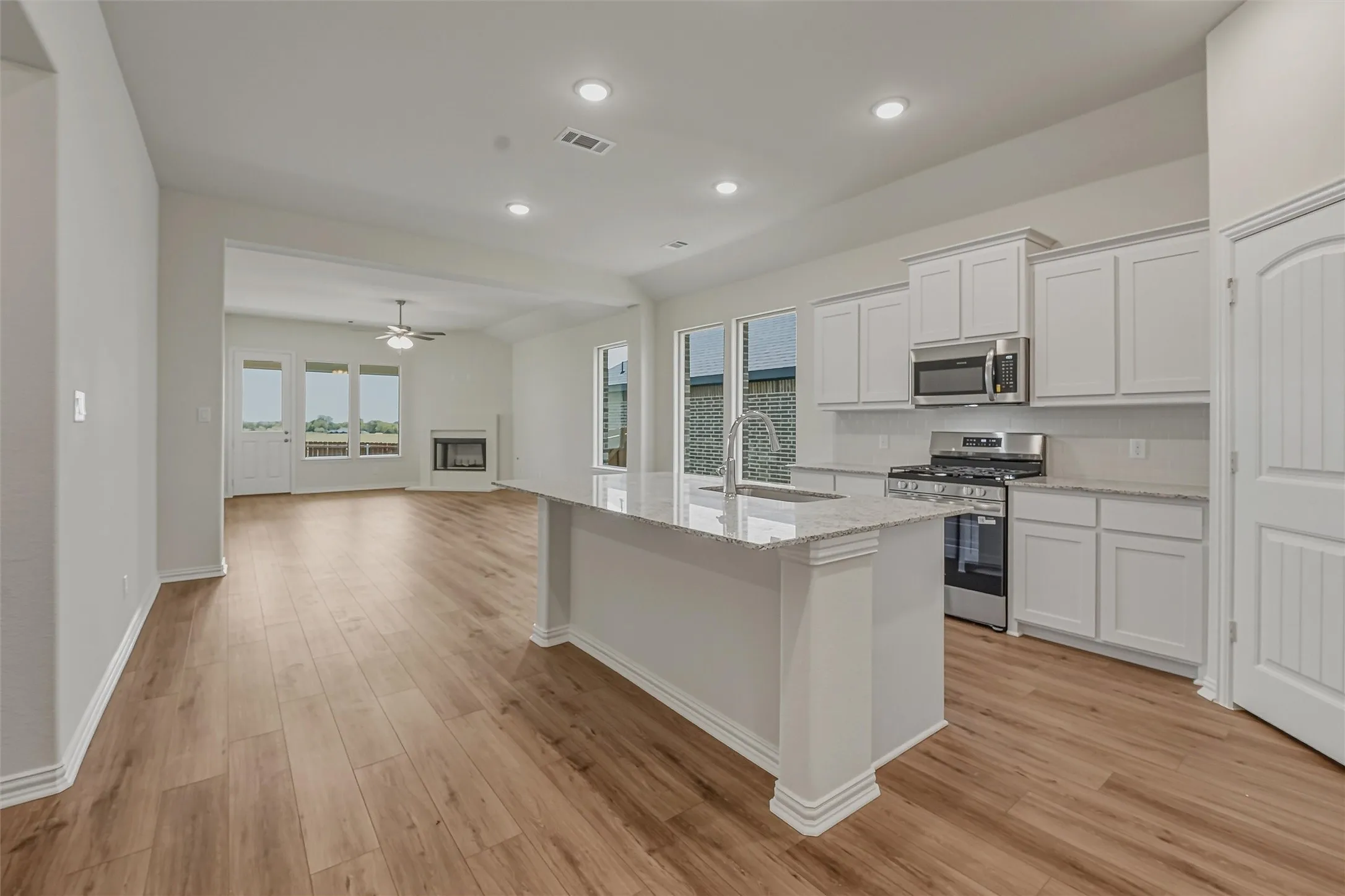 Open-concept kitchen featuring an island with a sink, white cabinetry, stainless steel appliances, and wood-finish flooring