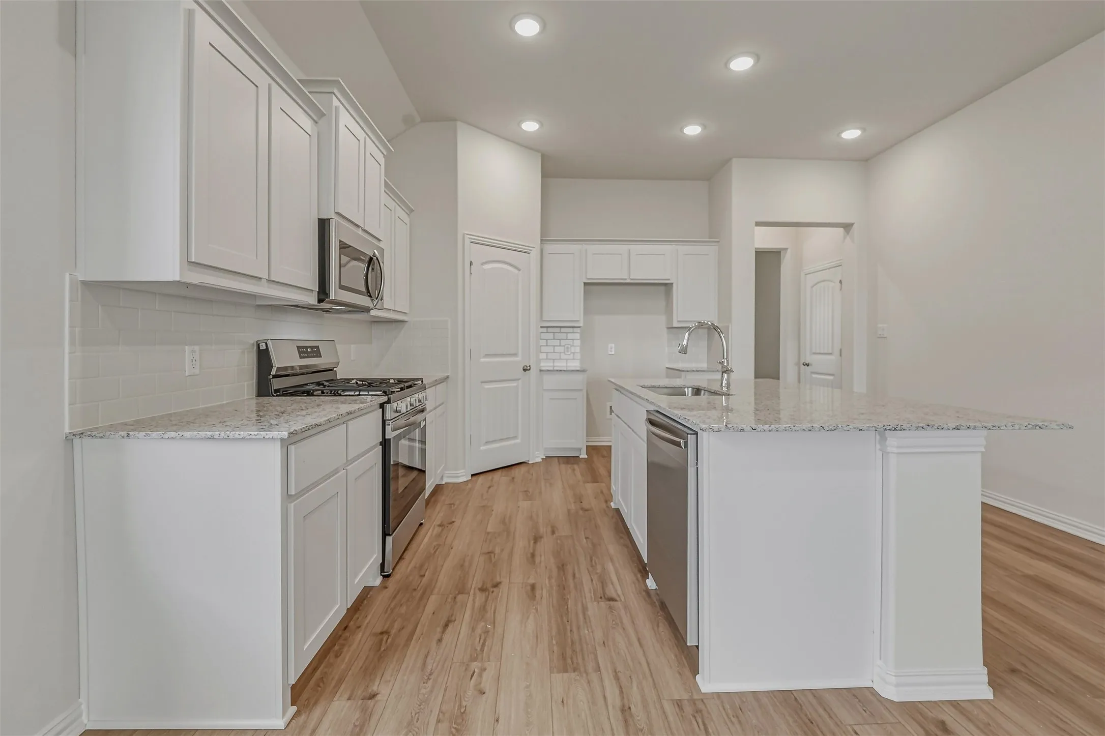 Kitchen featuring white shaker-style cabinetry, granite countertops, stainless steel appliances, wood-finish flooring, and recessed lighting