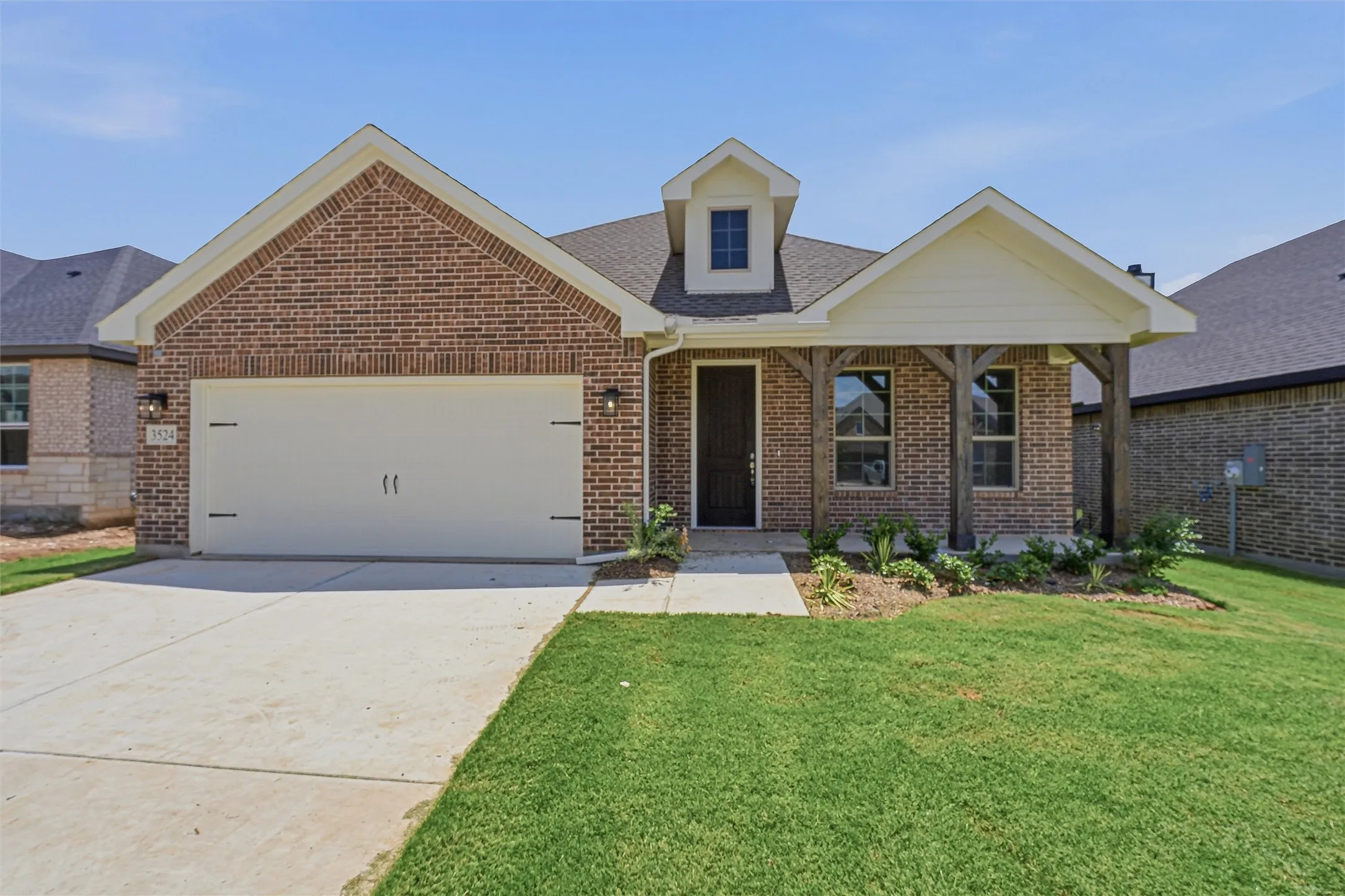Brick facade residence featuring a covered entry, decorative dormer, attached garage, concrete driveway, and a landscaped front yard with green lawn