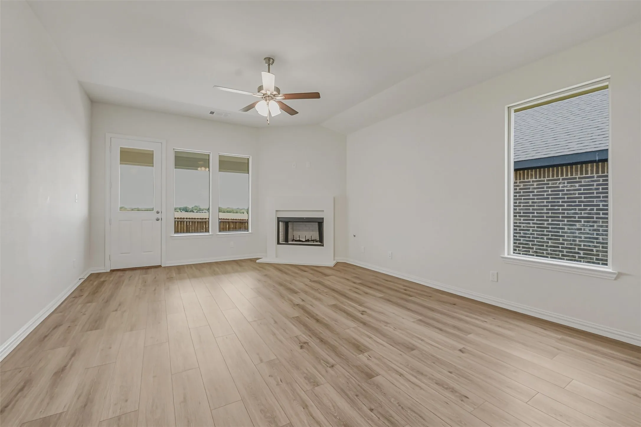 Spacious room featuring wood-finish flooring, a contemporary fireplace, and a ceiling fan with integrated lighting