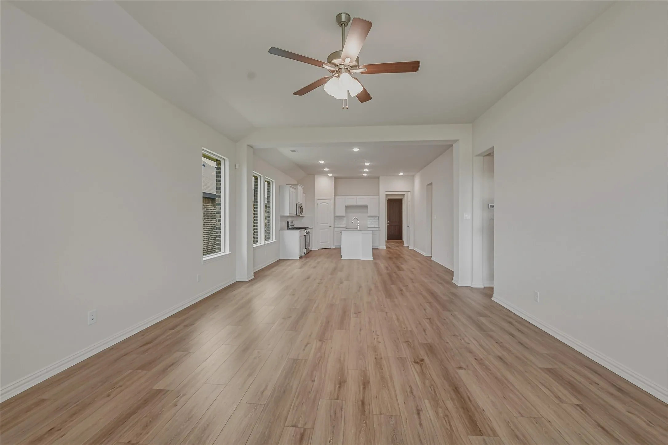 Spacious living area featuring wood-finish flooring, a ceiling fan with light, and recessed lighting