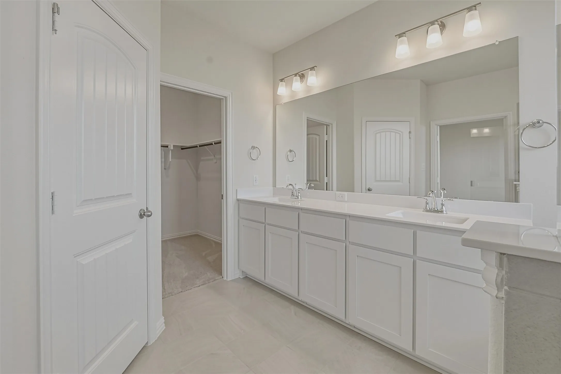 Dual vanity with white cabinetry, integrated sinks, chrome fixtures, and an expansive mirror