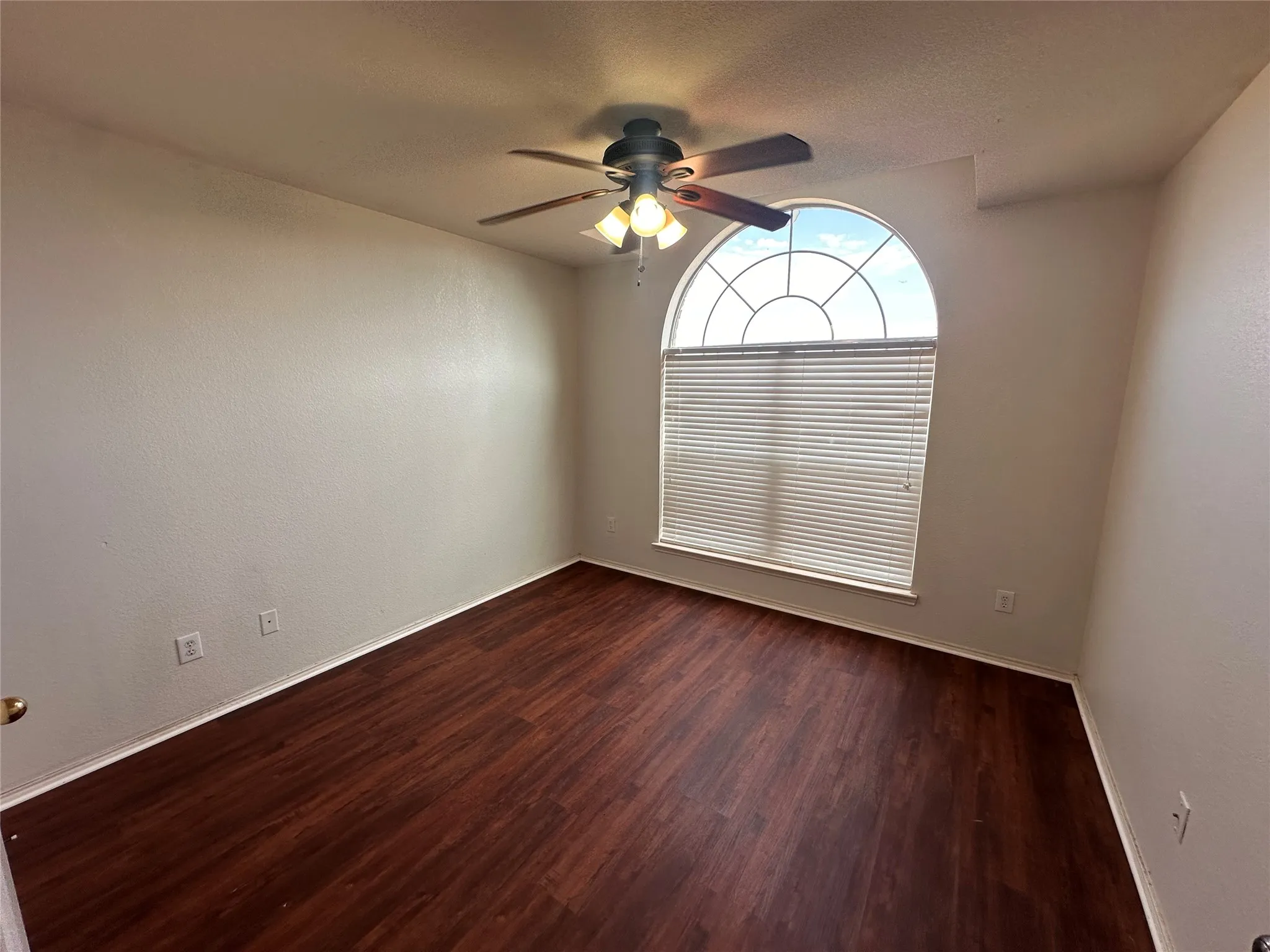 Hardwood-finish flooring, a large arched window with blinds, and a ceiling fan with integrated lighting