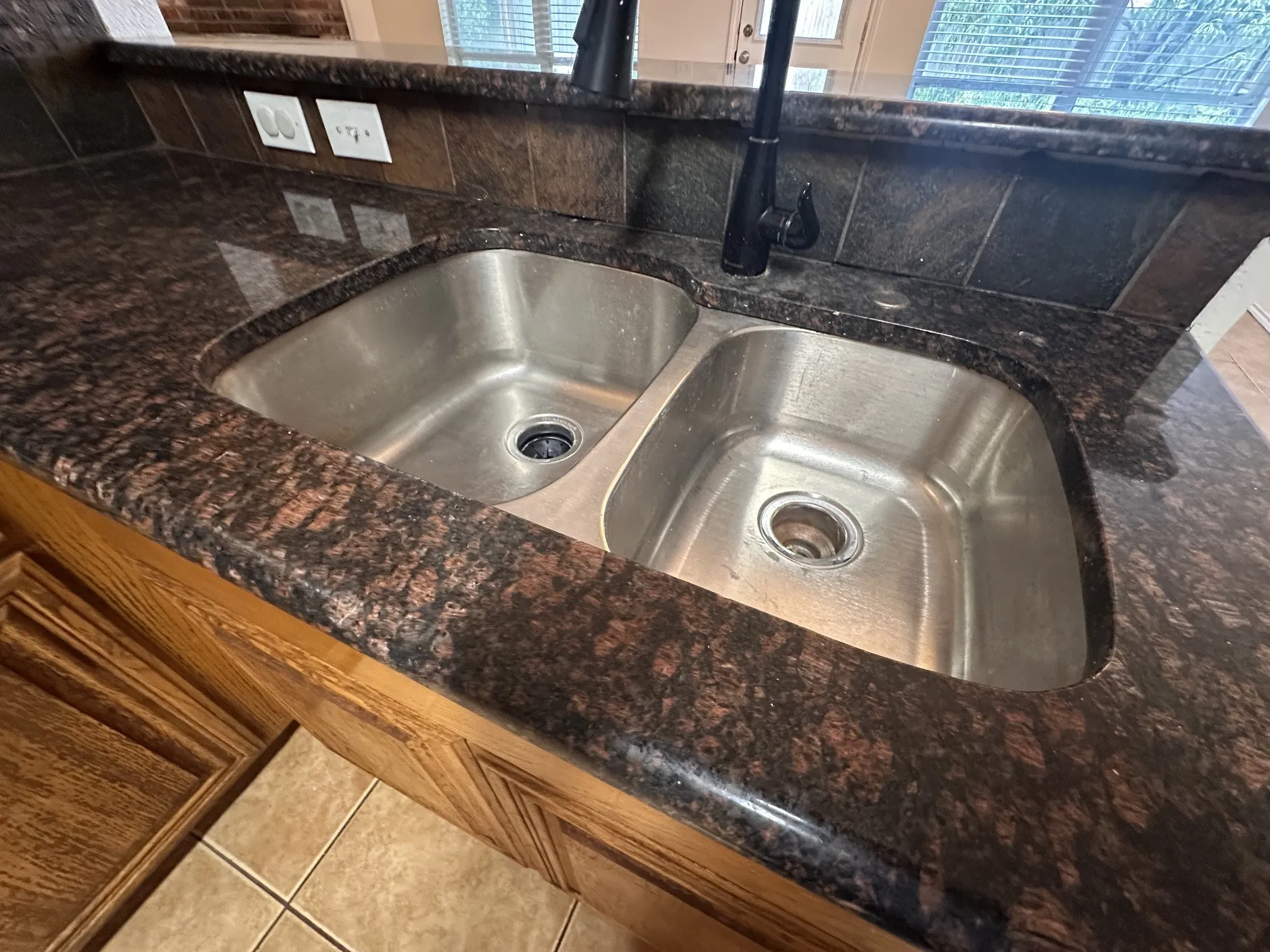 Dual basin stainless steel sink set within a granite countertop with integrated backsplash