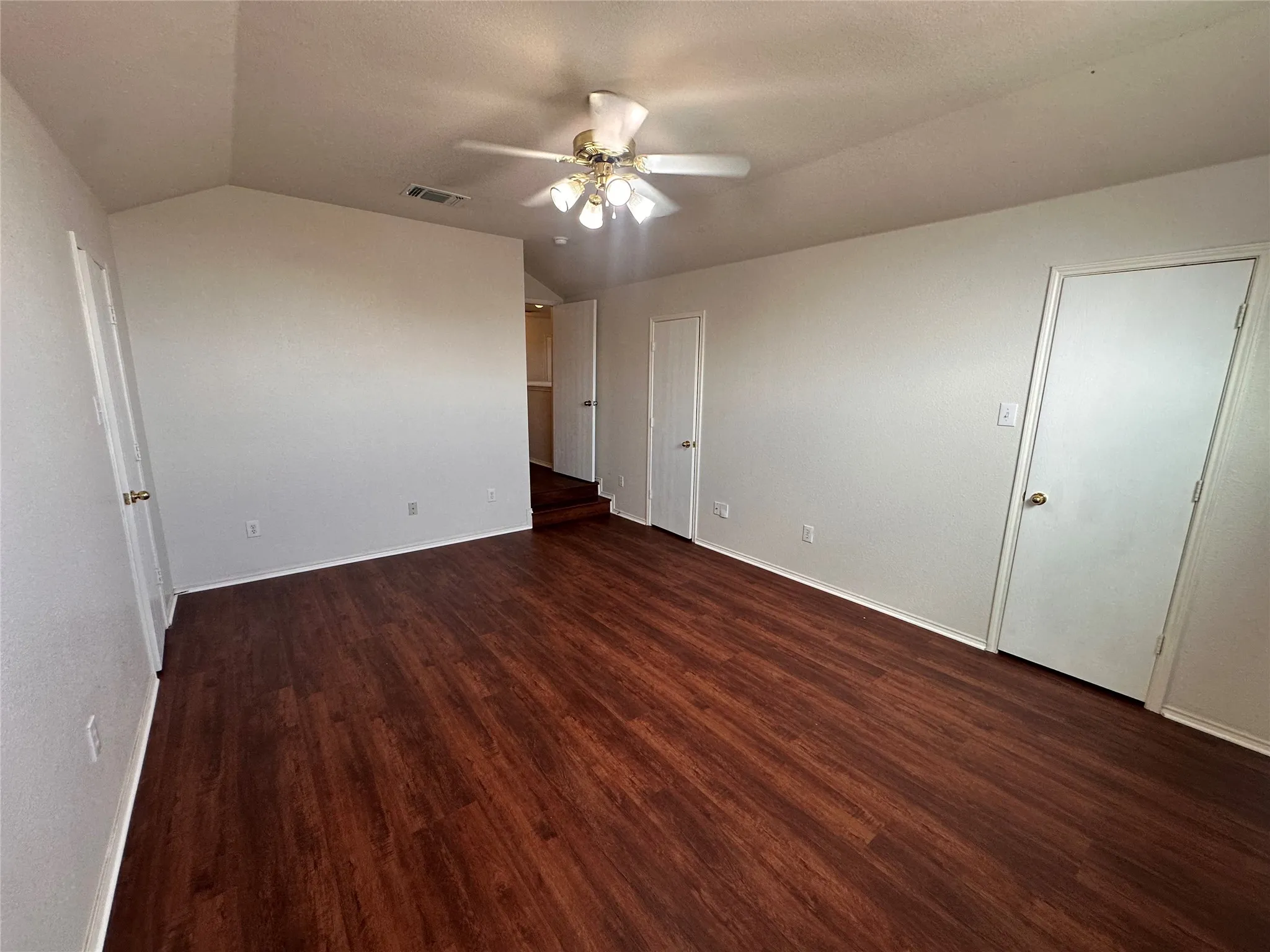 Vaulted ceiling with a ceiling fan light fixture, wood-finish flooring, white walls, and white trim