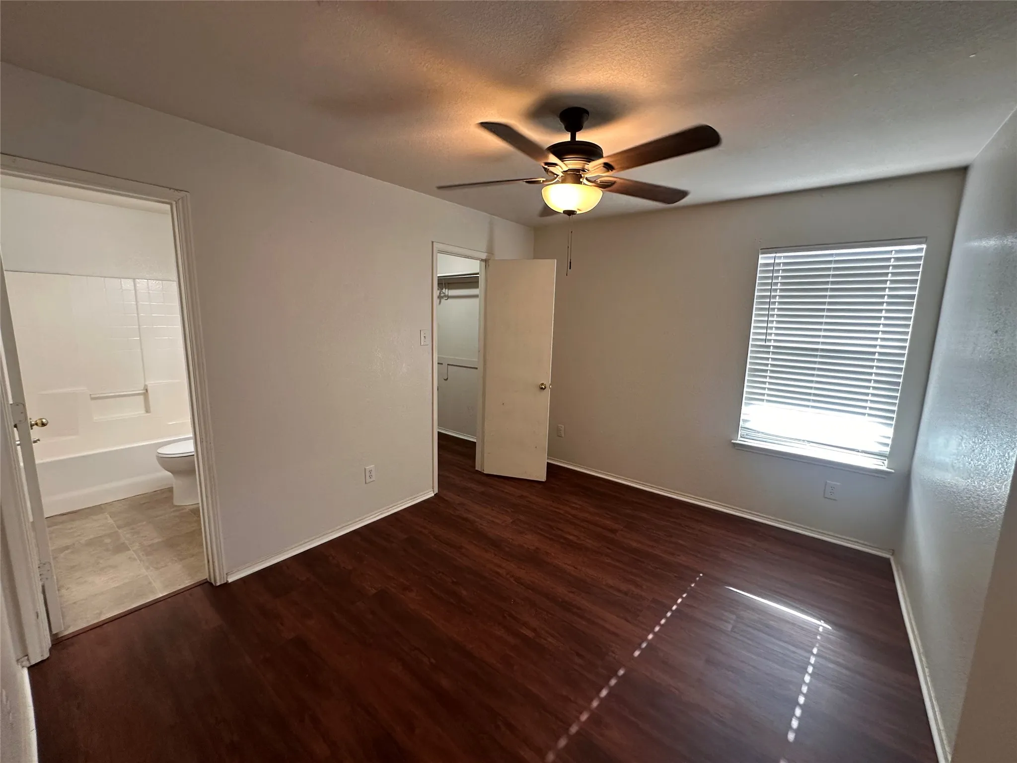 Wood-finish flooring, ceiling fan with integrated lighting, window with blinds, and white interior doors