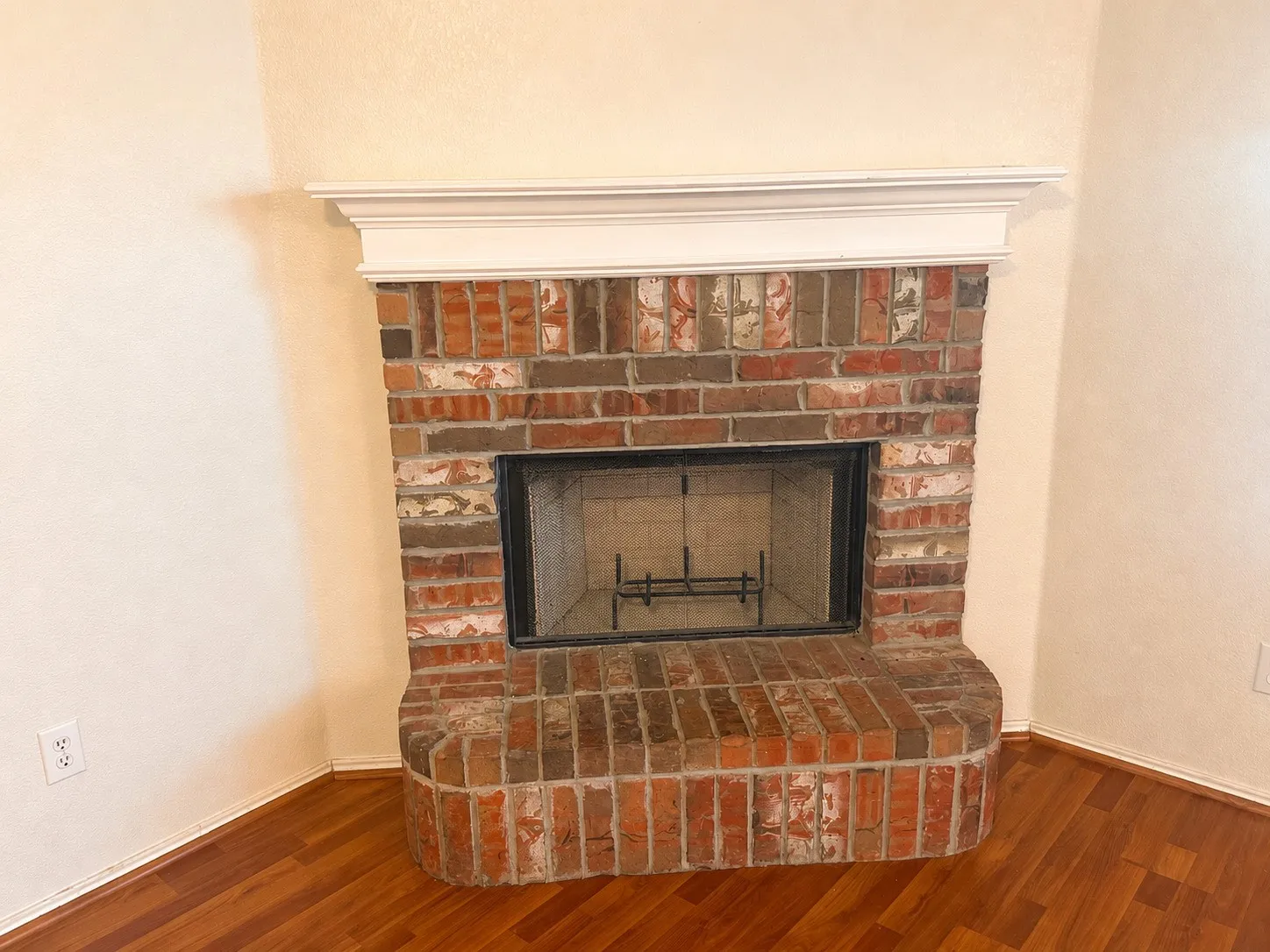 Corner brick fireplace with a white mantelpiece and a metal fire grate