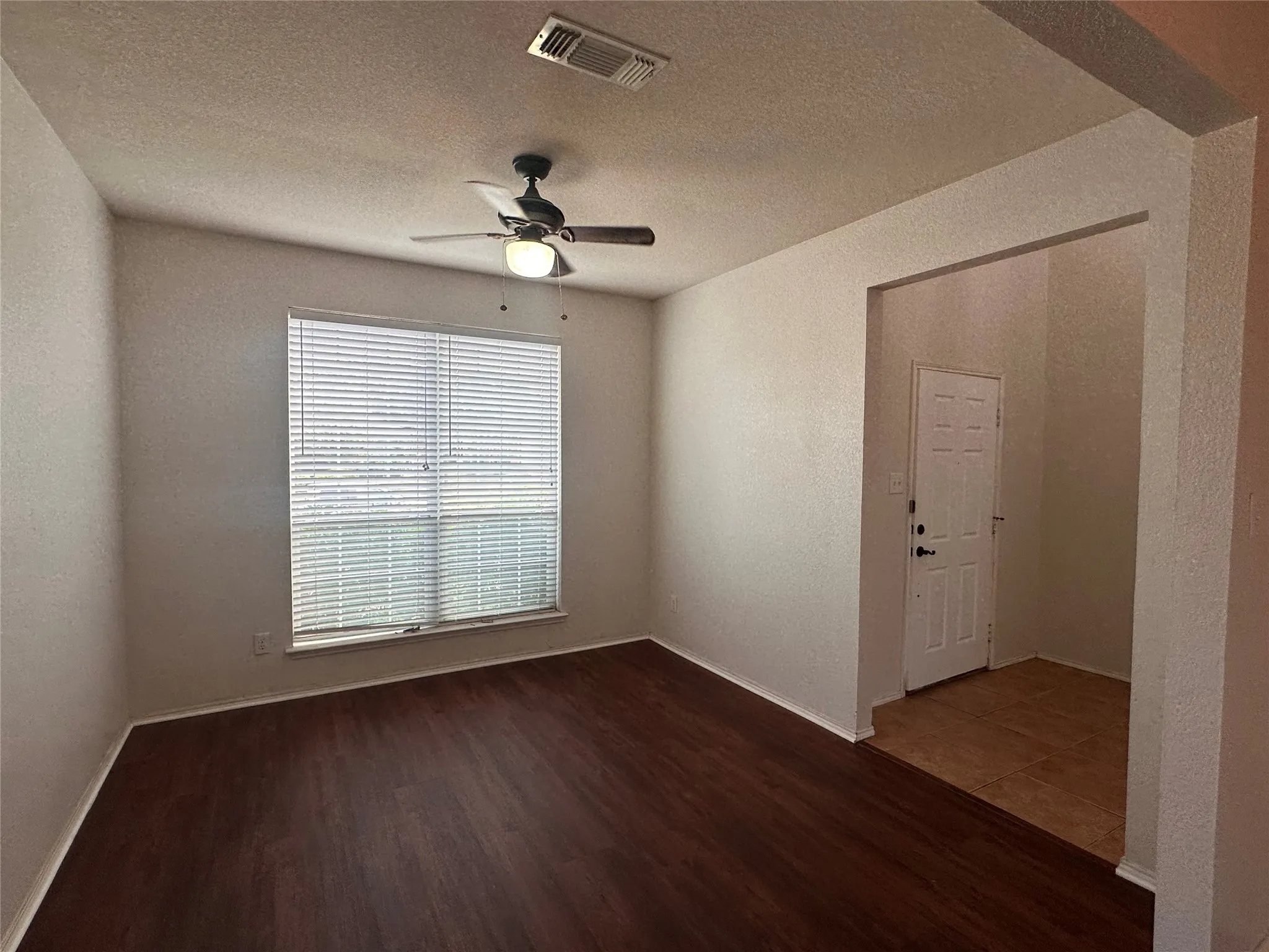Wood-finish flooring, ceiling fan with integrated lighting, large window with blinds, tiled entry