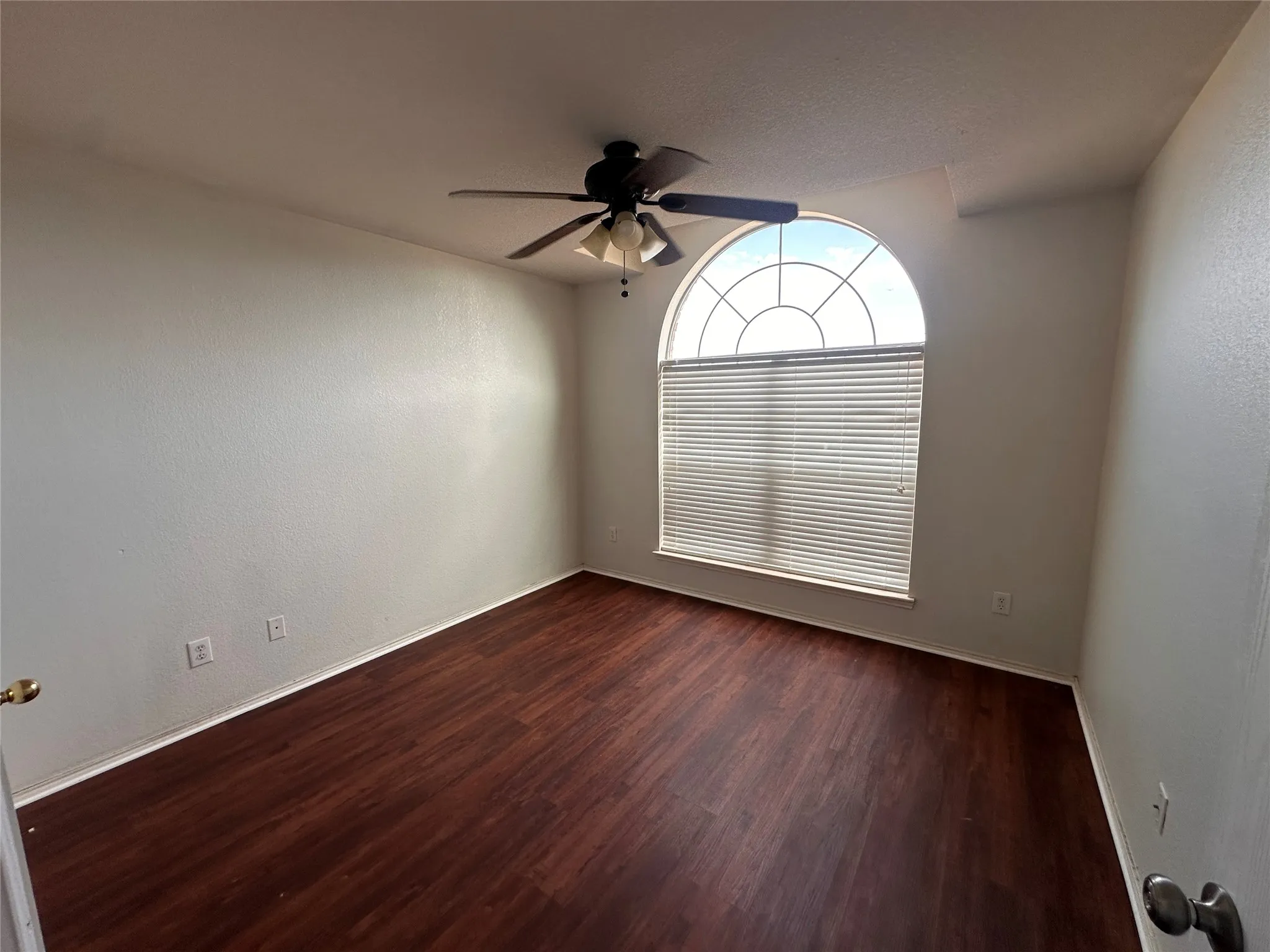 Arch-top window with blinds, dark wood-finish flooring, and ceiling fan with integrated lighting