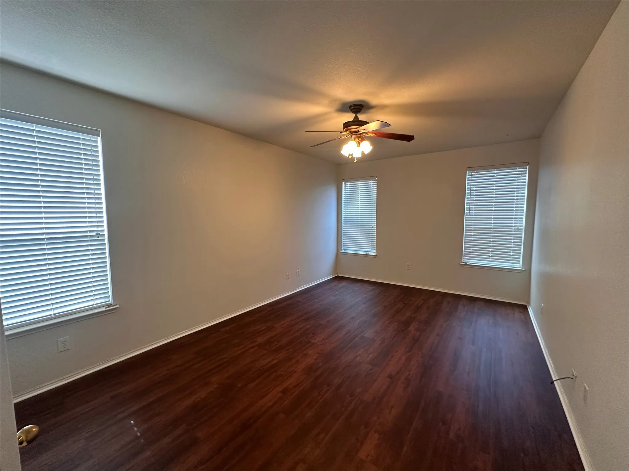 Spacious room featuring wood-finish flooring, multiple windows with blinds, and a ceiling fan with integrated lighting