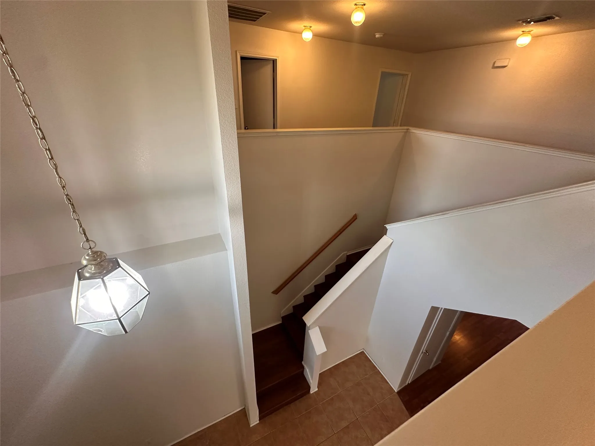 Multi-level interior with wood-finish stairs, tile flooring, and a decorative pendant light fixture